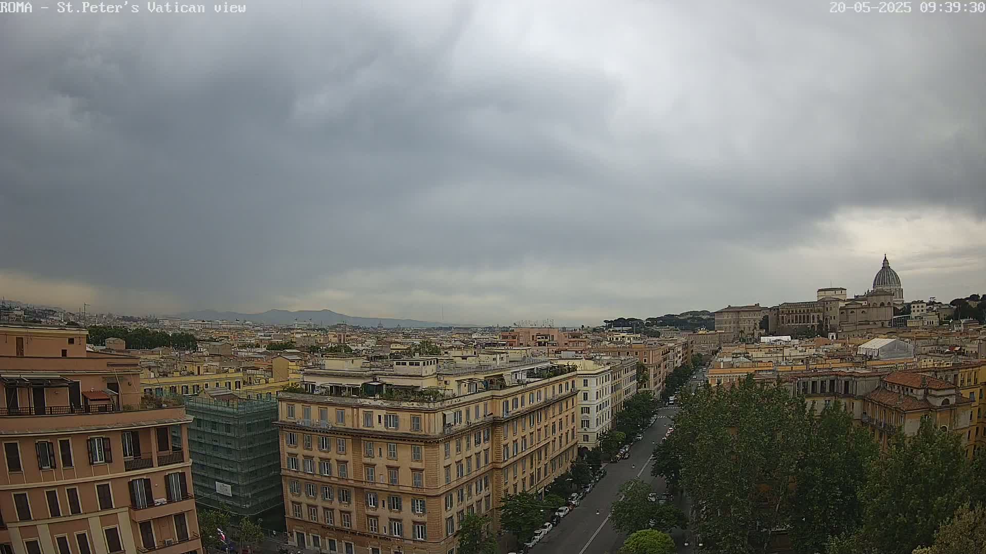 A wide shot of a cityscape under an overcast sky shows multi-story buildings, a street, and trees, with a large dome visible in the distance.
