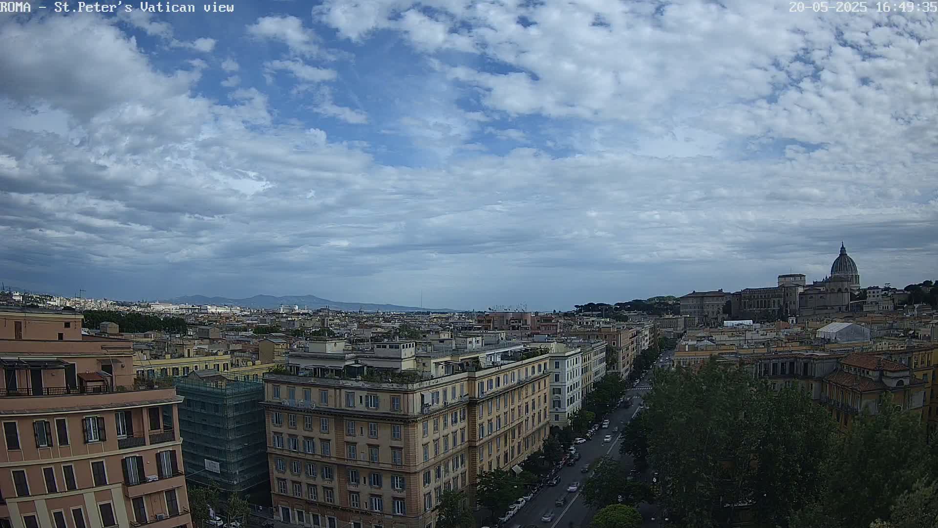 A partly cloudy sky overlooks a cityscape with a large basilica and dome in the distance, showing a street with cars and numerous buildings.