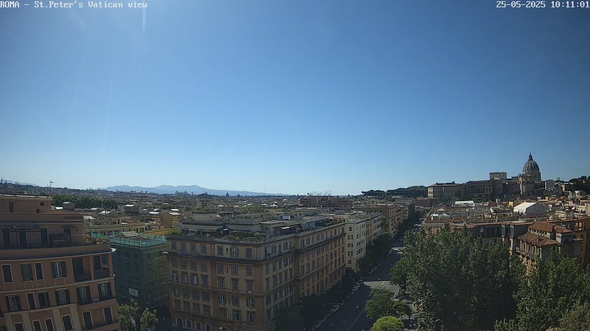 A high-angle, long shot on a clear, sunny day shows a cityscape with the dome of St. Peter's Basilica visible in the distance.