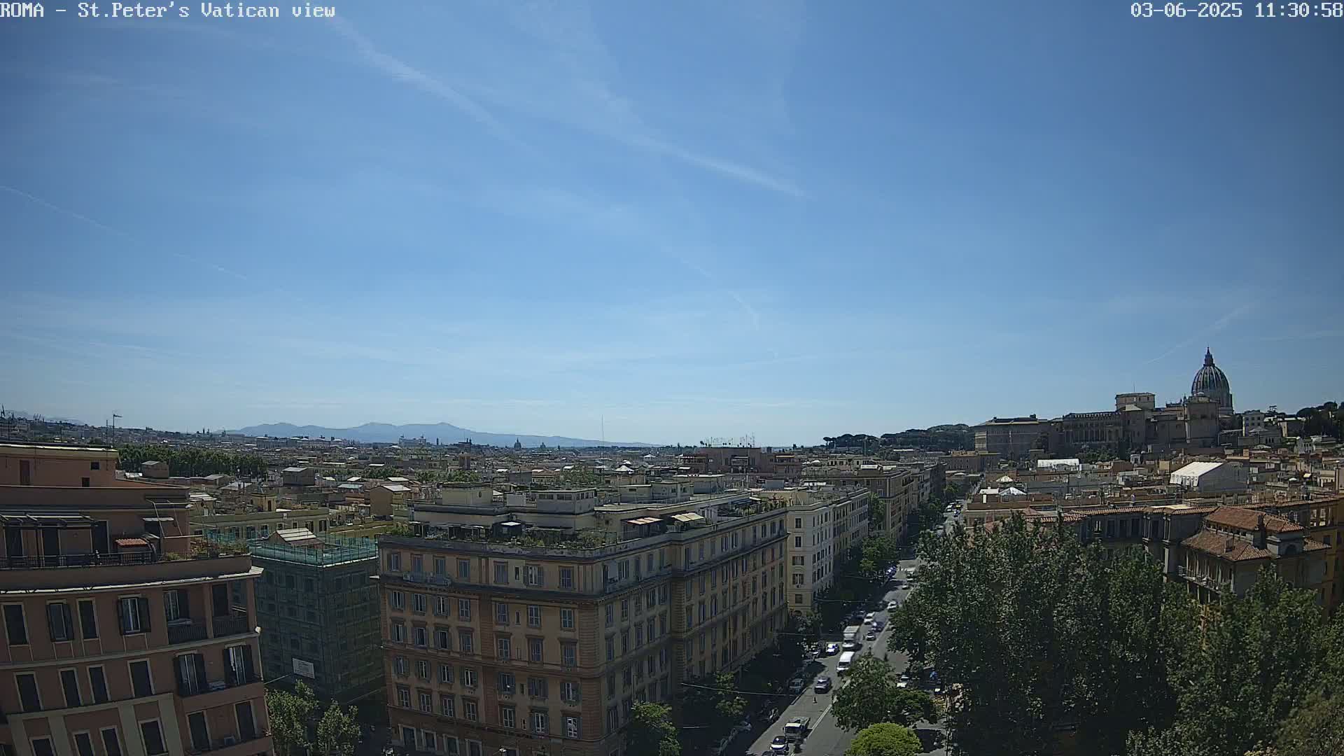 A sunny cityscape view shows a distant basilica with a dome, city buildings, a street with cars, and mountains on the horizon.