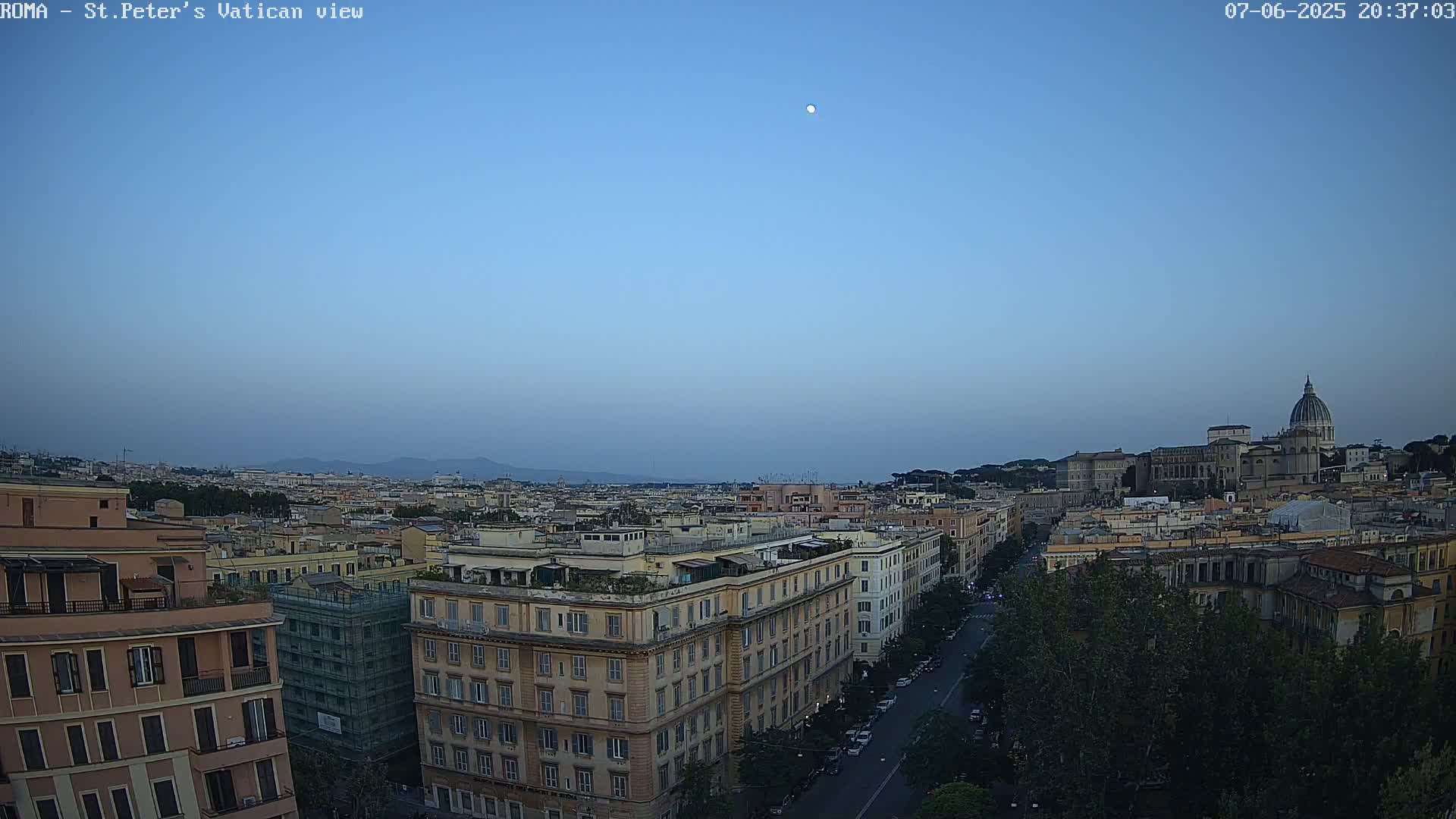 A high-angle, twilight view of Rome, Italy, shows the city skyline, including St. Peter's Basilica in the distance under a clear, moonlit sky.