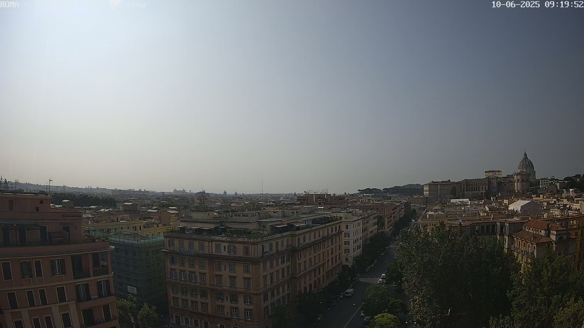 A hazy, sunny day reveals an aerial view of Rome, showcasing a cityscape of buildings extending to a distant horizon where St. Peter's Basilica is visible.