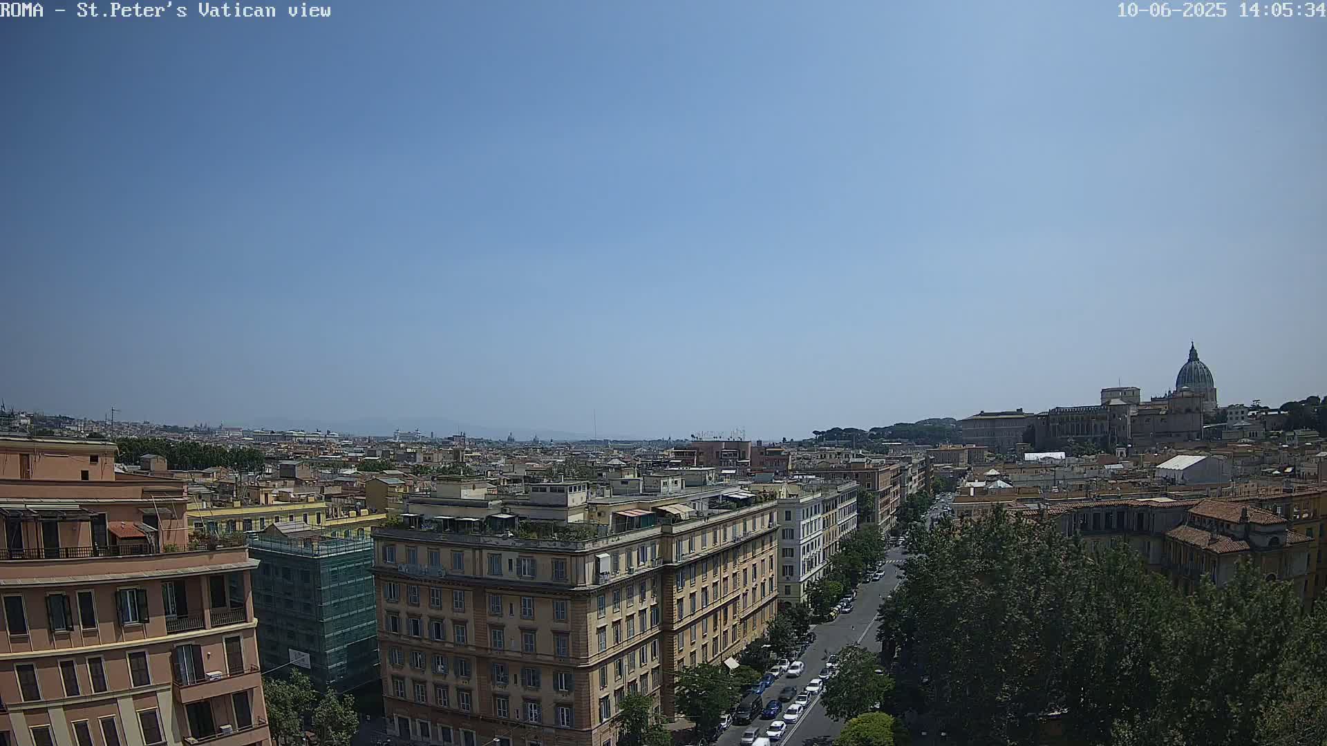 A high-angle, long shot on a clear, sunny day shows a cityscape with a large building and dome in the distance, and several city blocks of buildings closer to the viewer.