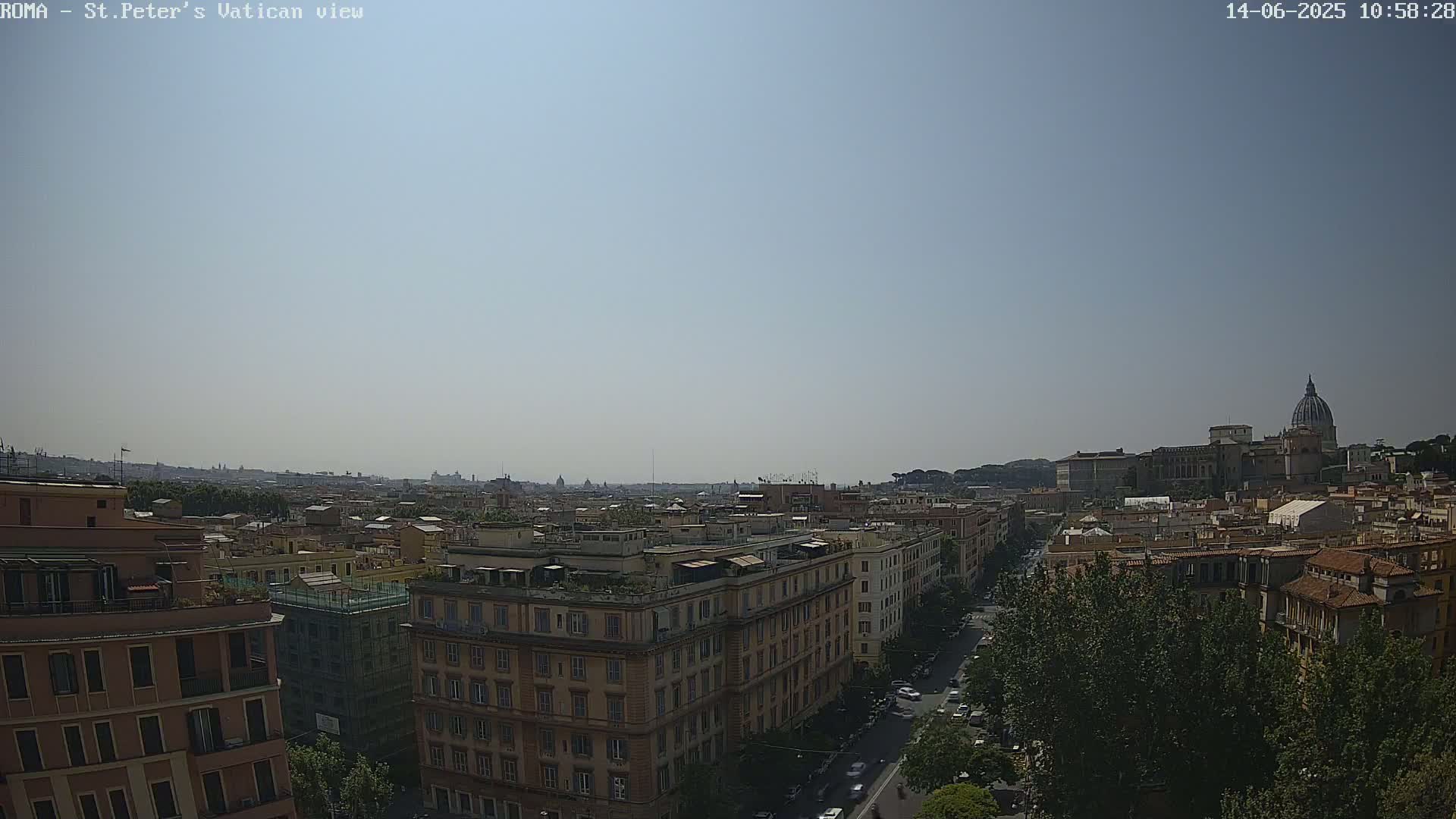 A distant view of a city skyline on a clear, sunny day, featuring a large dome-shaped building, numerous other buildings, and a street with traffic.