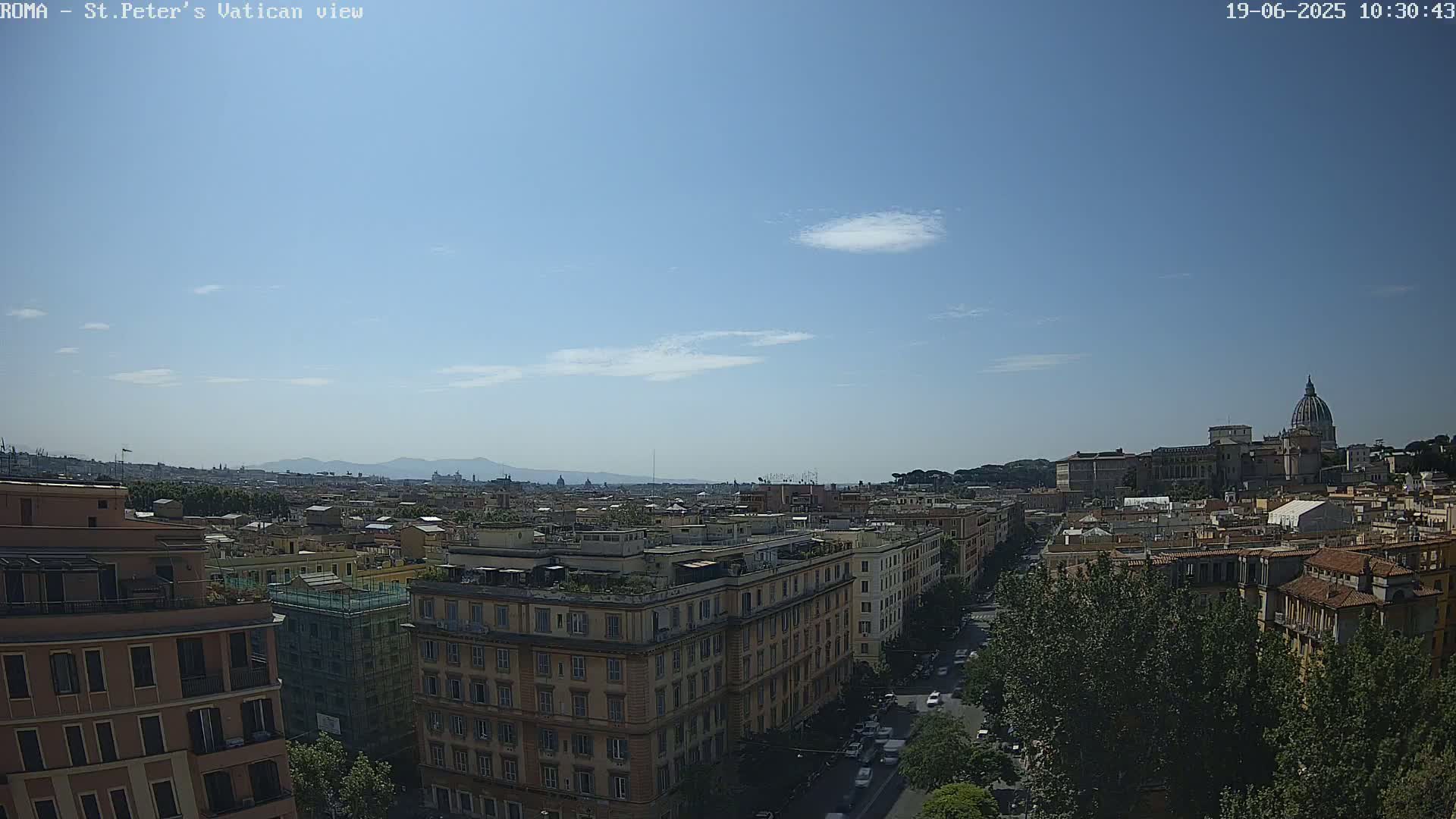 A mostly sunny cityscape view shows distant mountains, a city street, numerous buildings, and the dome of a large building in the background.