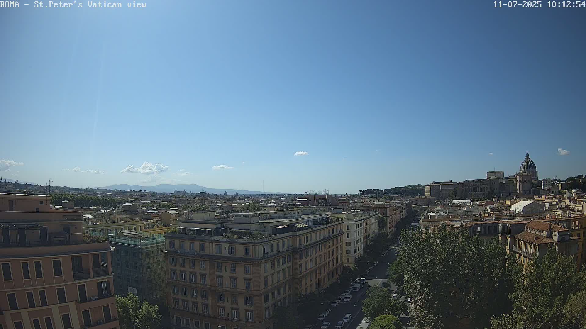 A sunny cityscape view shows a distant basilica with a dome, and many buildings stretching to distant mountains under a mostly clear sky.