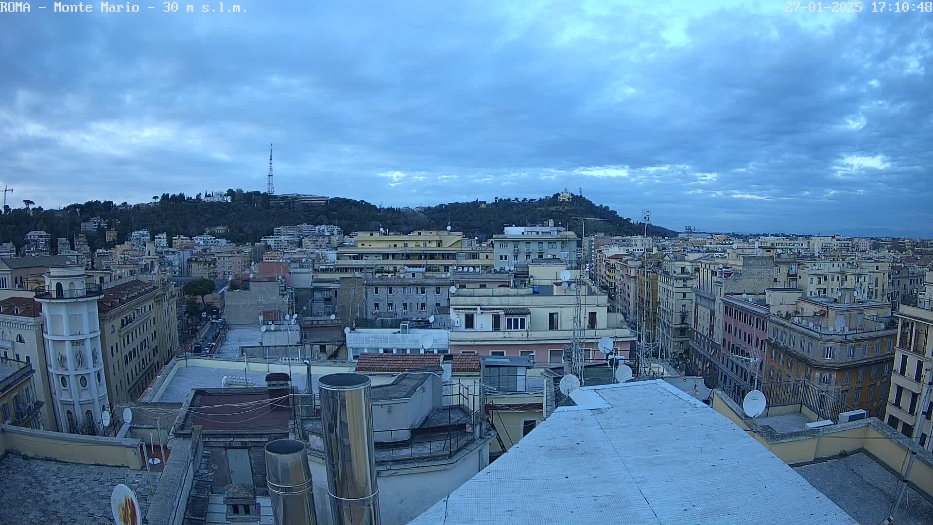 A panoramic view of a city under a cloudy sky shows many buildings extending to a hill in the distance.