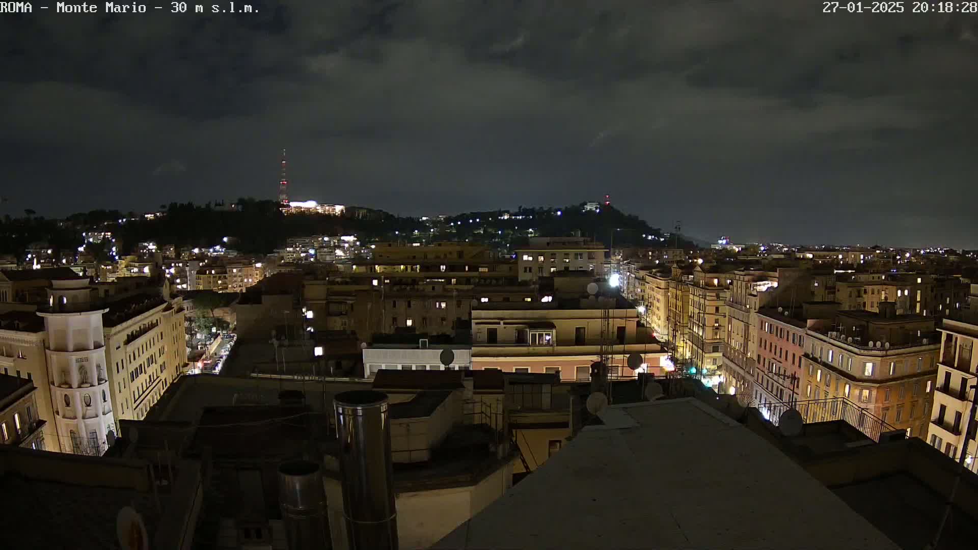 A nighttime view of a city illuminated with streetlights under a dark, cloudy sky.