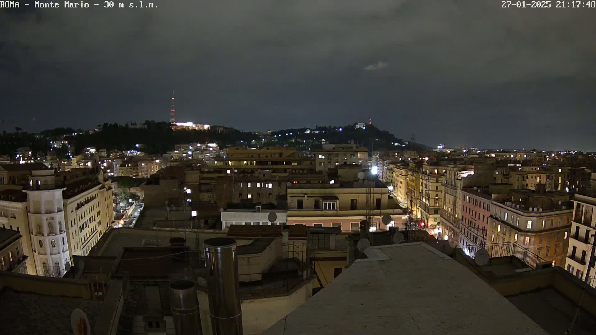 A nighttime view of a city, showing numerous buildings illuminated under a dark, cloudy sky.