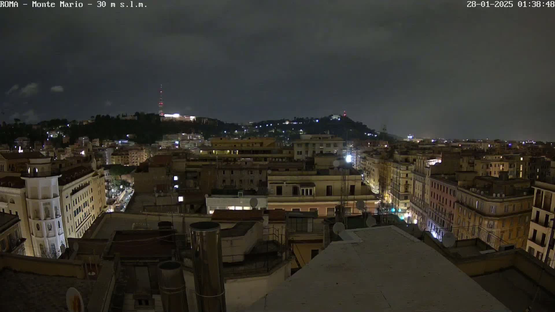 A nighttime view of a city skyline, showing numerous buildings illuminated under a dark, cloudy sky.