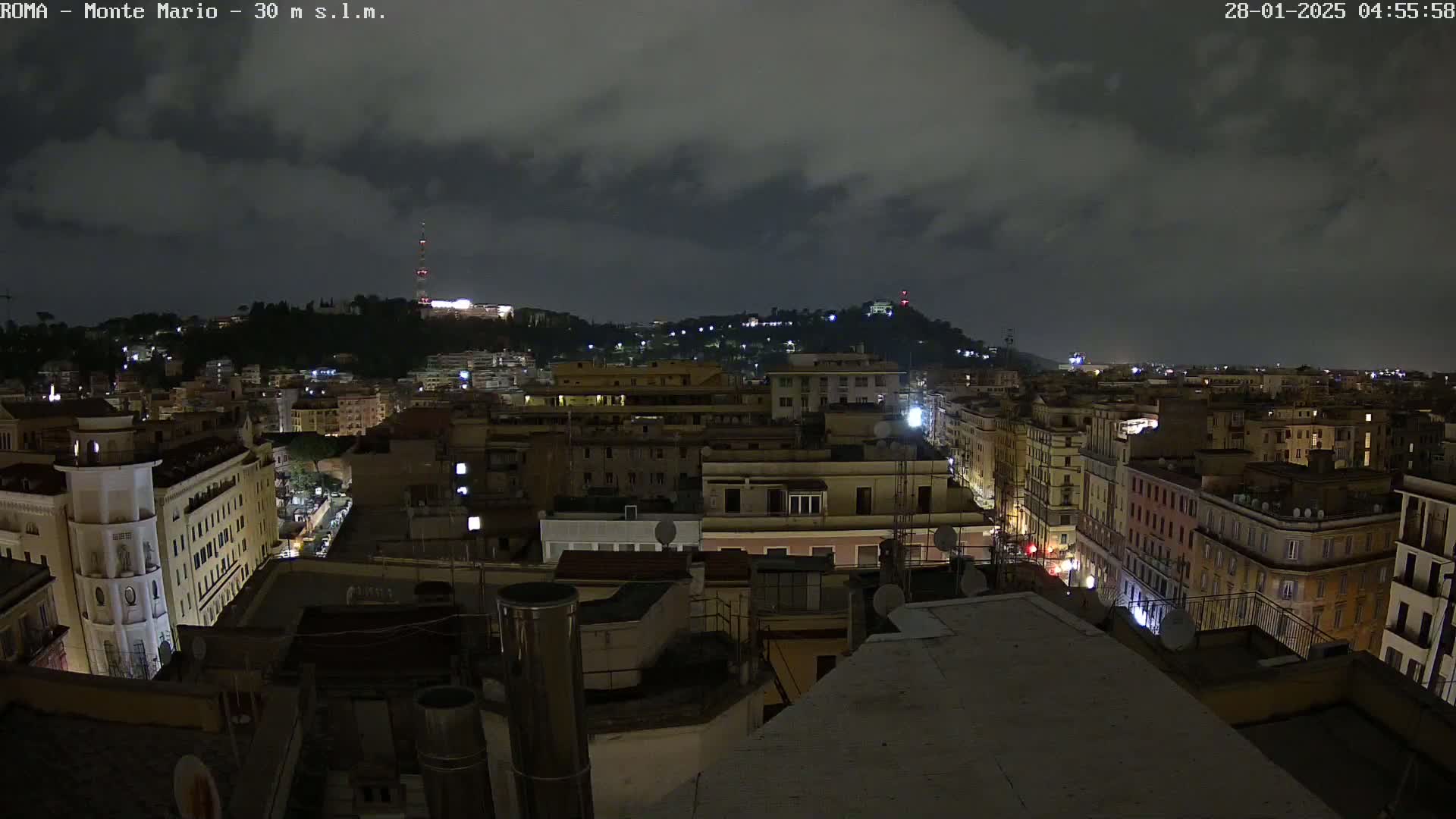 A nighttime view of a city, under a cloudy sky, shows a sprawling cityscape with illuminated buildings and streets.