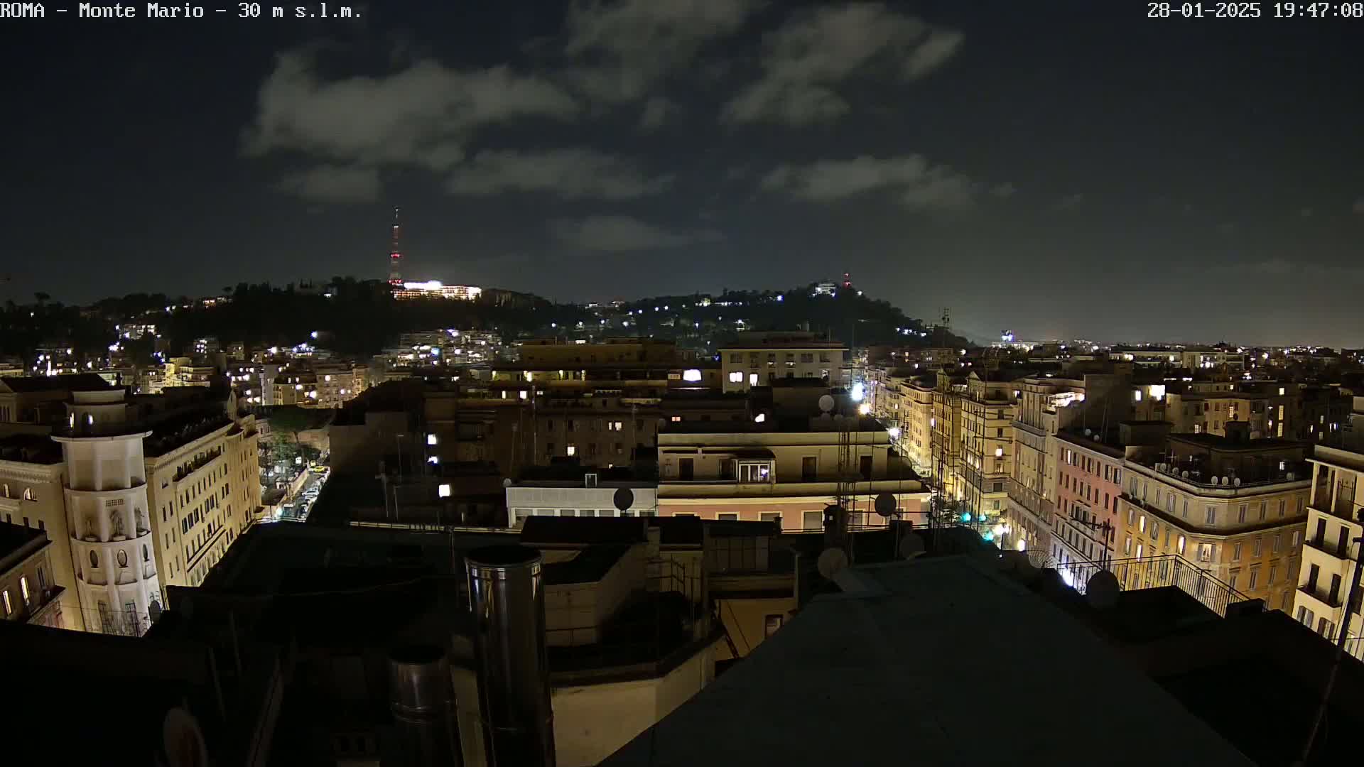 A nighttime view of a city with buildings illuminated, under a partly cloudy sky.