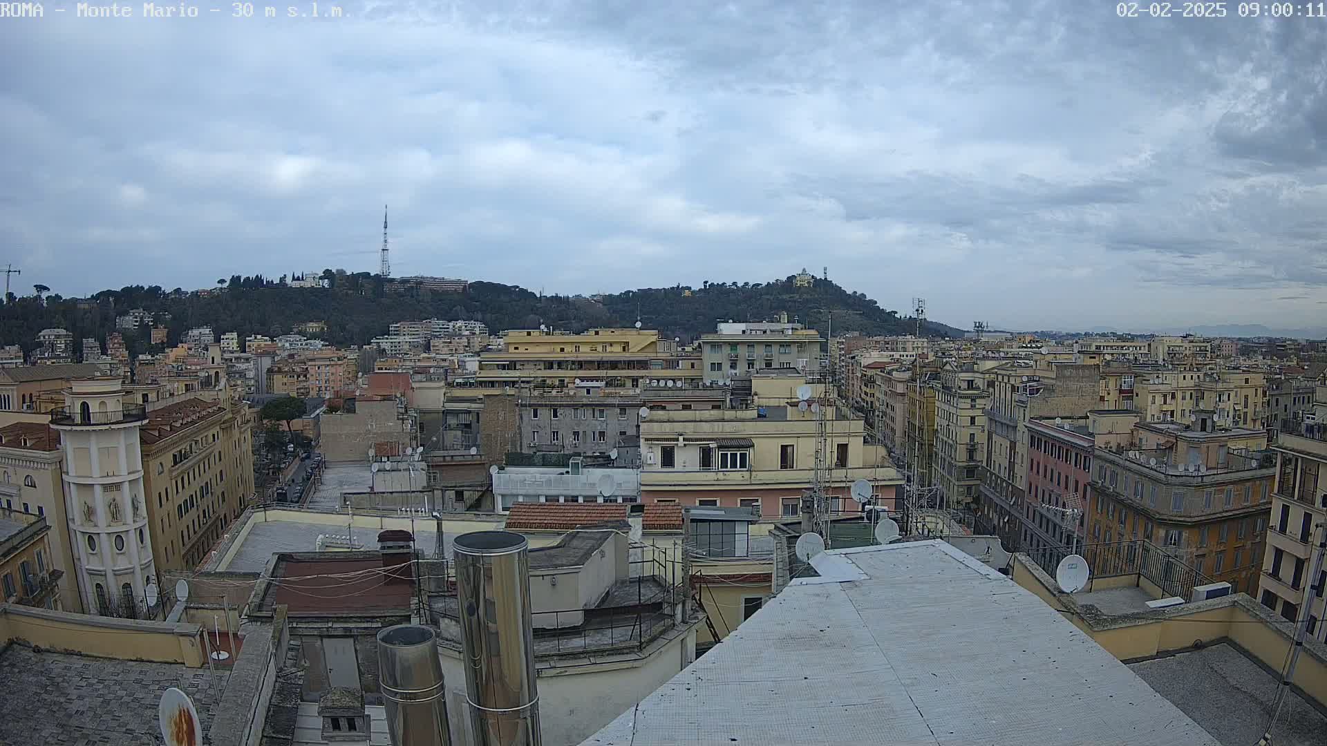 A cloudy day reveals a cityscape of numerous multi-story buildings, with a hill in the background.