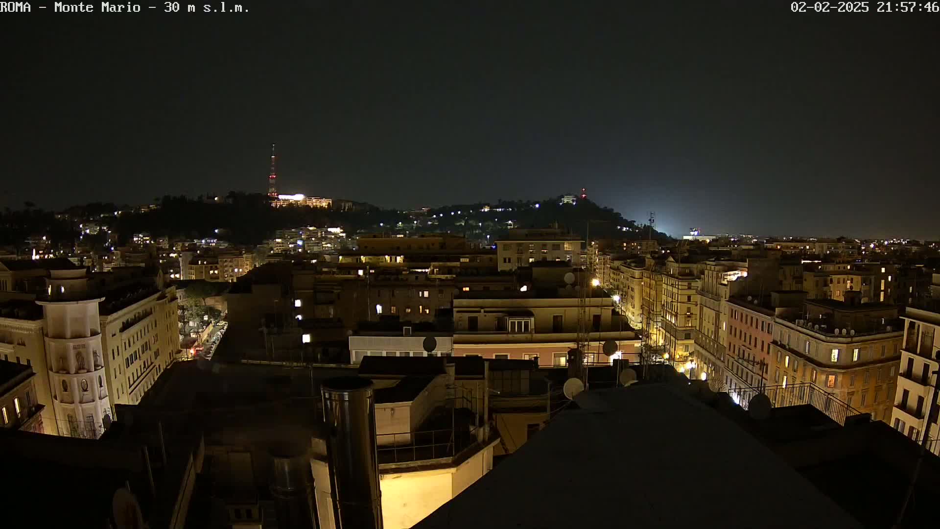 A nighttime aerial view of a city shows numerous buildings illuminated against a dark sky.