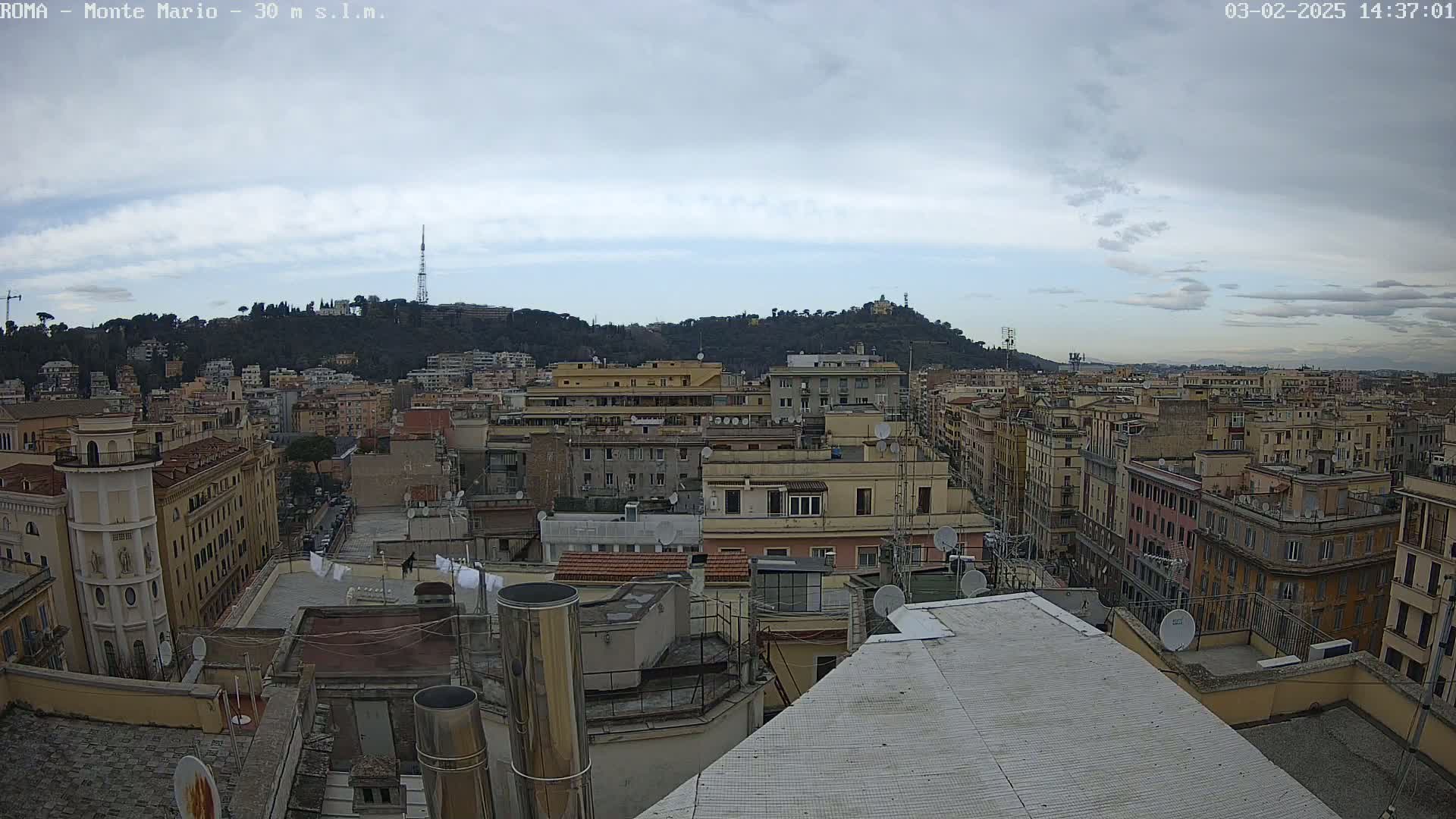 A cloudy cityscape view shows numerous buildings and a hill in the distance.