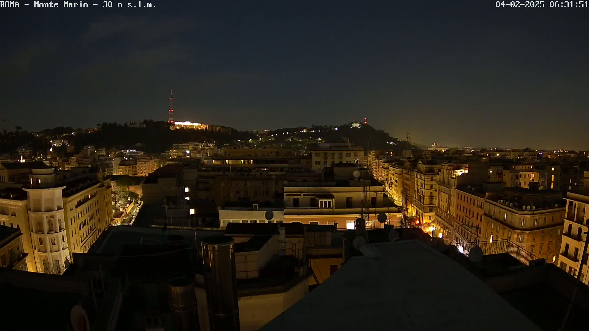 A nighttime aerial view of a city, with hills in the background under a clear, dark sky.