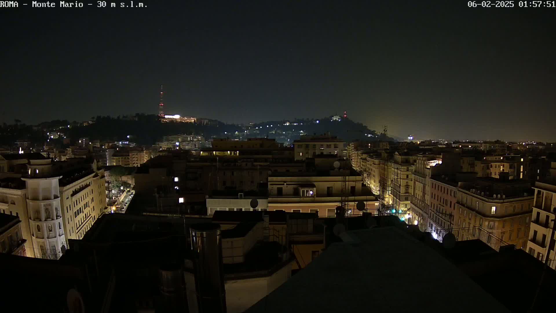 A nighttime cityscape view shows a hilltop in the distance, illuminated buildings and streets below, and a dark sky.