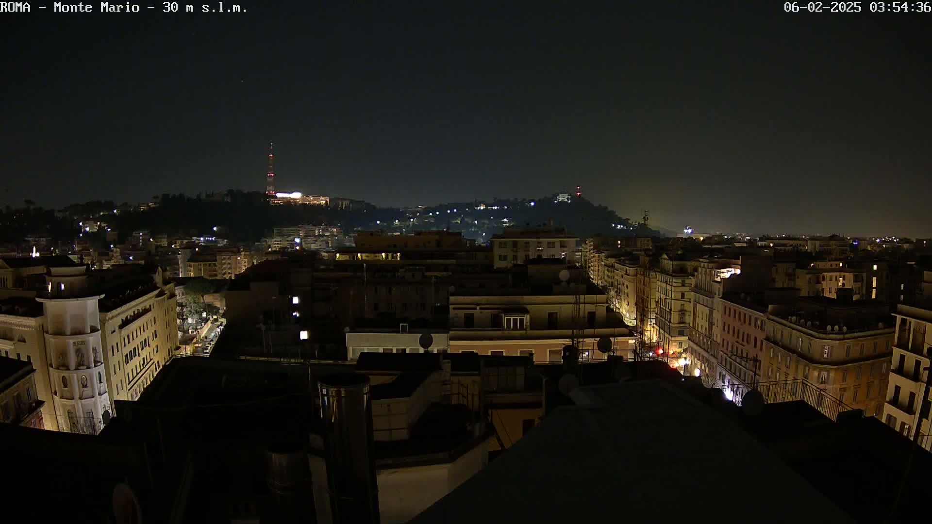 A nighttime view of a city, showing a sprawling cityscape with dimly lit buildings and streets, under a clear, dark sky.