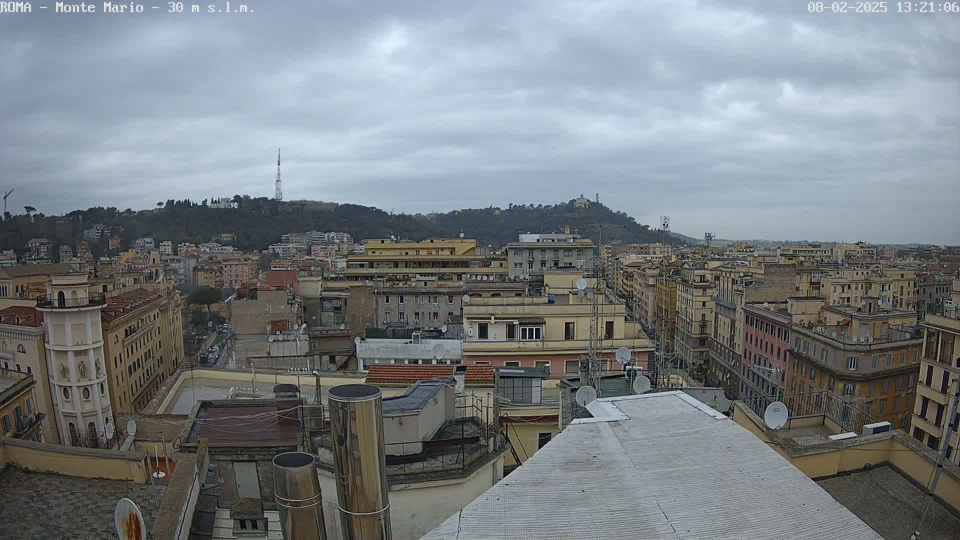 A panoramic view of a city under a cloudy sky, showing numerous buildings stretching to a hill in the distance.