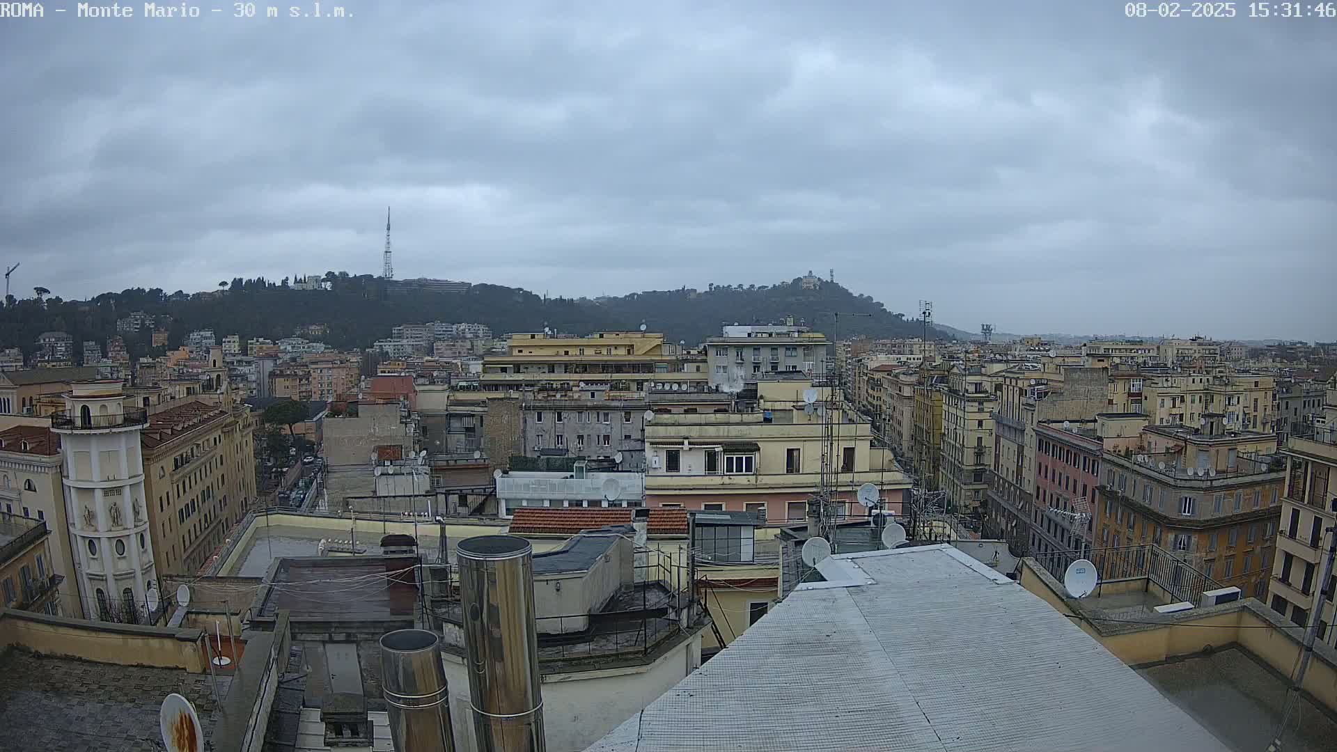 A city skyline under an overcast sky is viewed from a rooftop, showing numerous buildings and a distant hill.