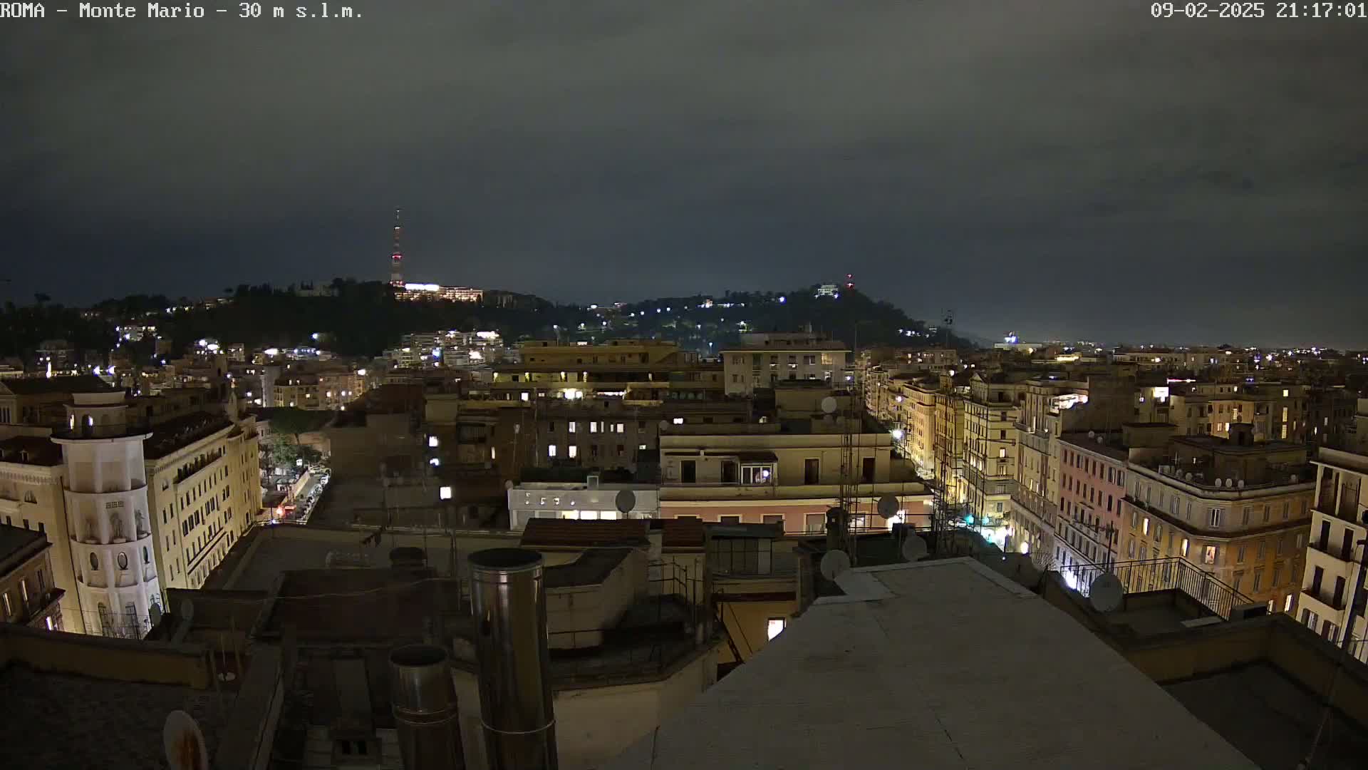 A nighttime view of a city illuminated by streetlights and building lights under a dark, cloudy sky.