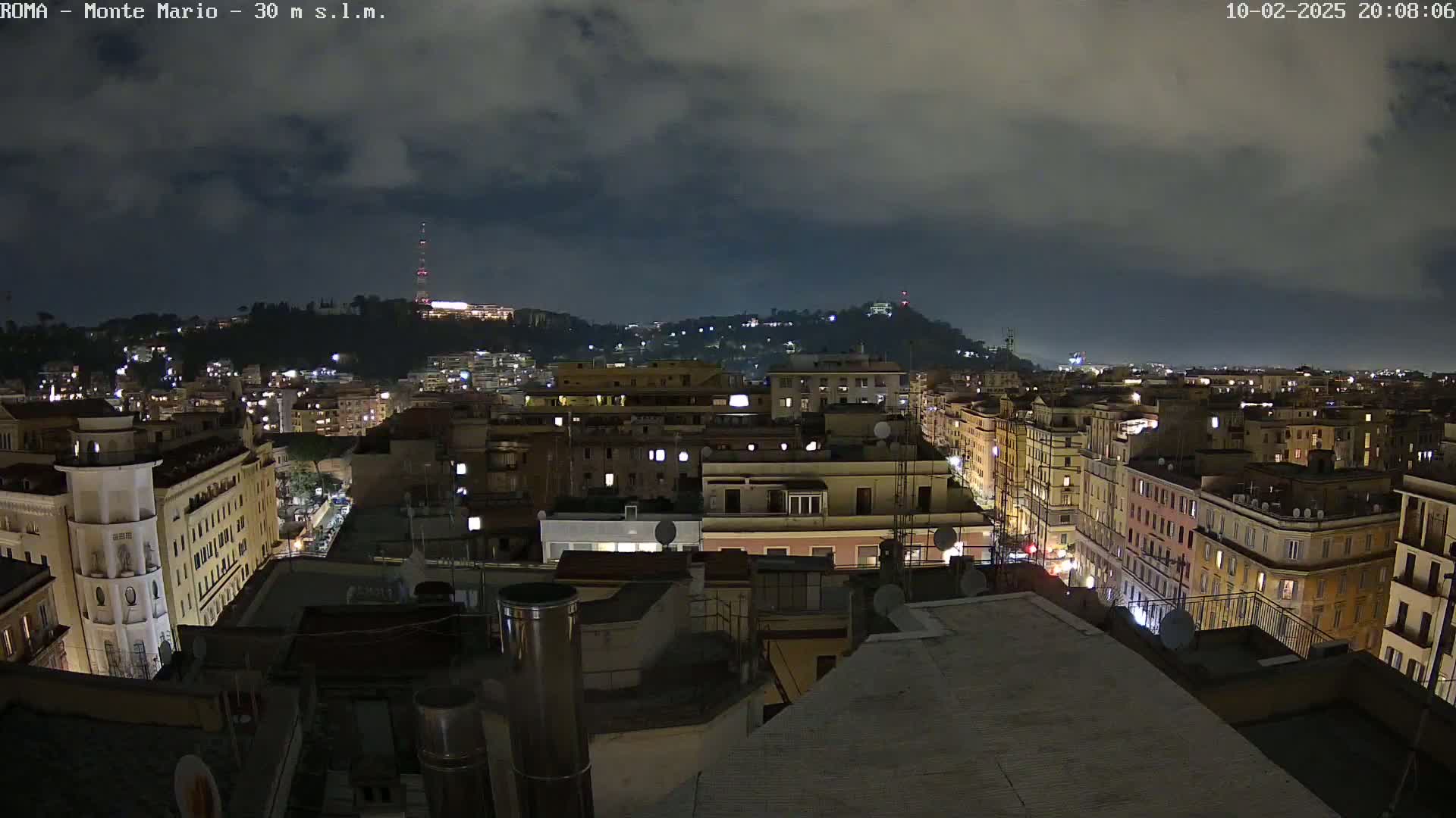 A nighttime view of a city illuminated by streetlights and building lights under a cloudy sky.