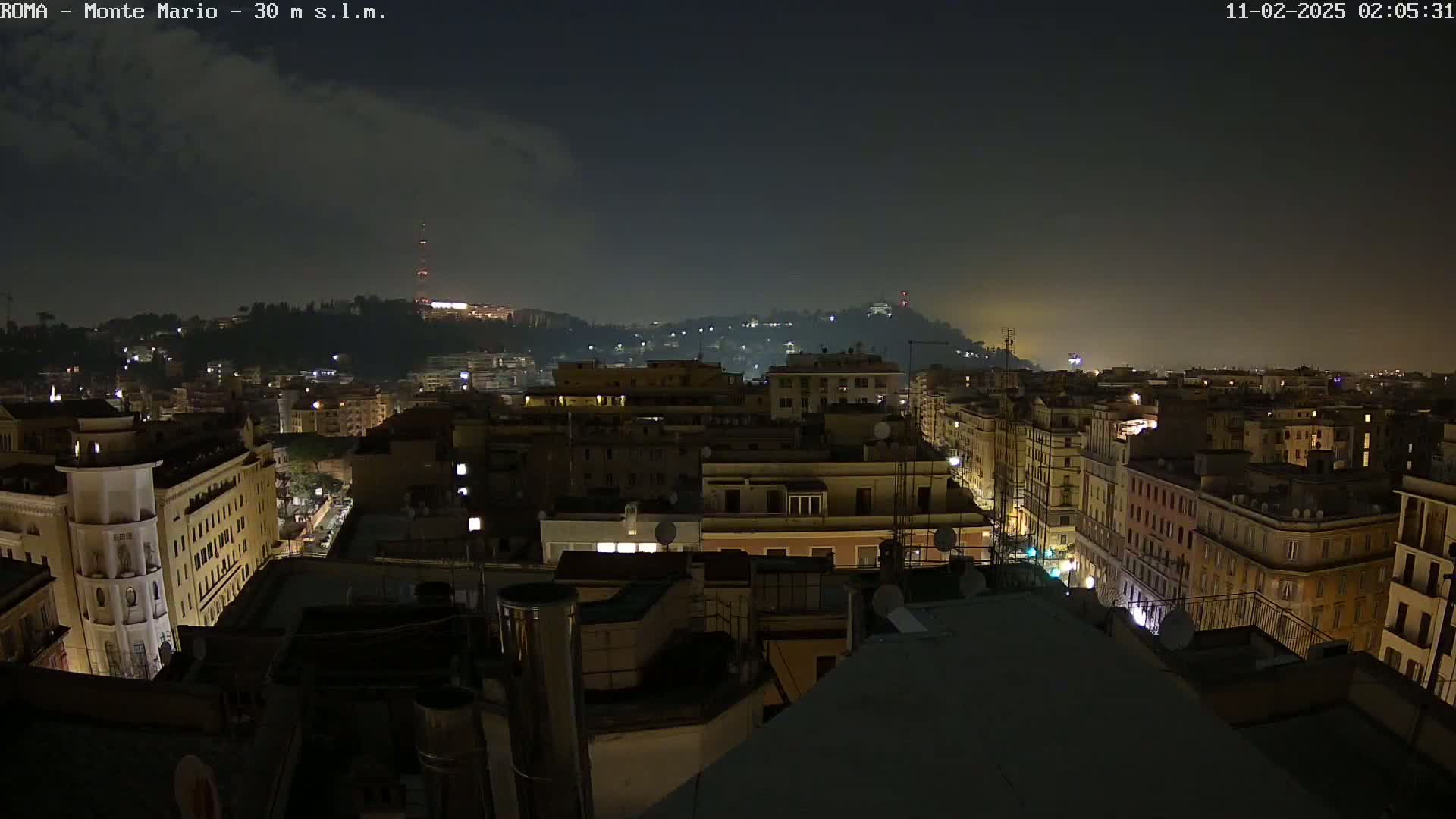 A nighttime, slightly hazy view of a city, with illuminated buildings stretching into the distance, extending up a hill.