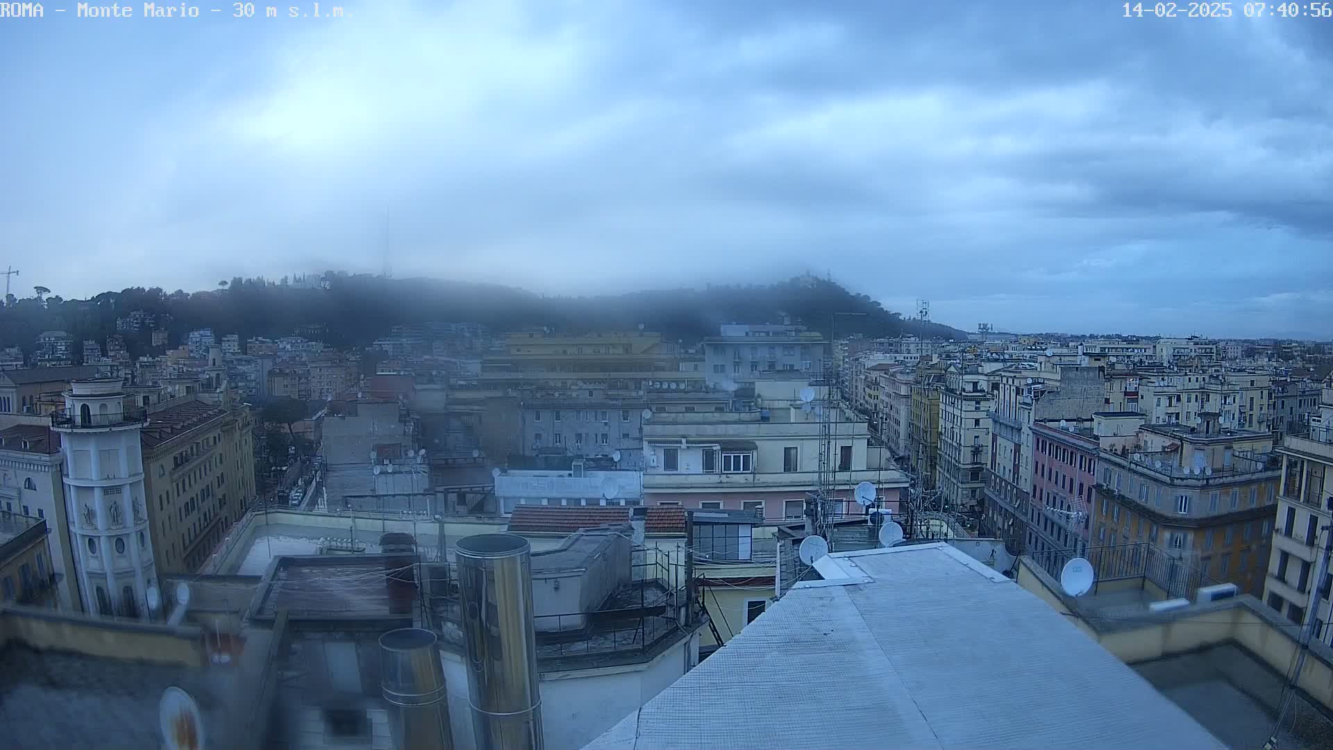 A city skyline is seen on an overcast day, with a hill shrouded in fog in the background.