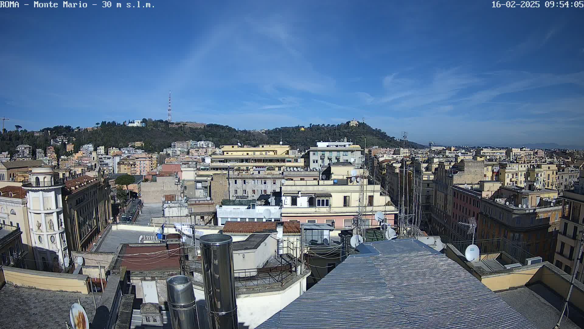 A sunny day reveals a panoramic view of rooftops and multi-story buildings, extending to a hill in the background.