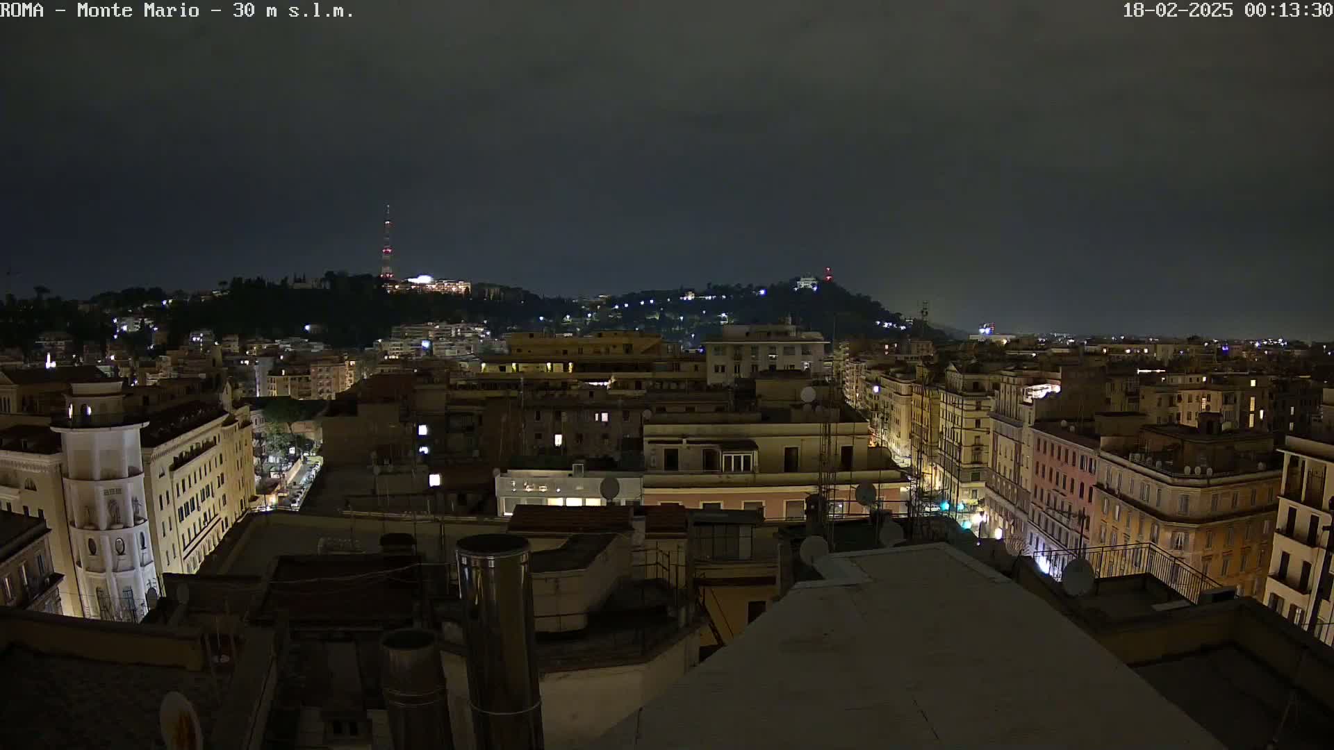 A nighttime view of a city, showing numerous buildings illuminated with streetlights under a dark, overcast sky.
