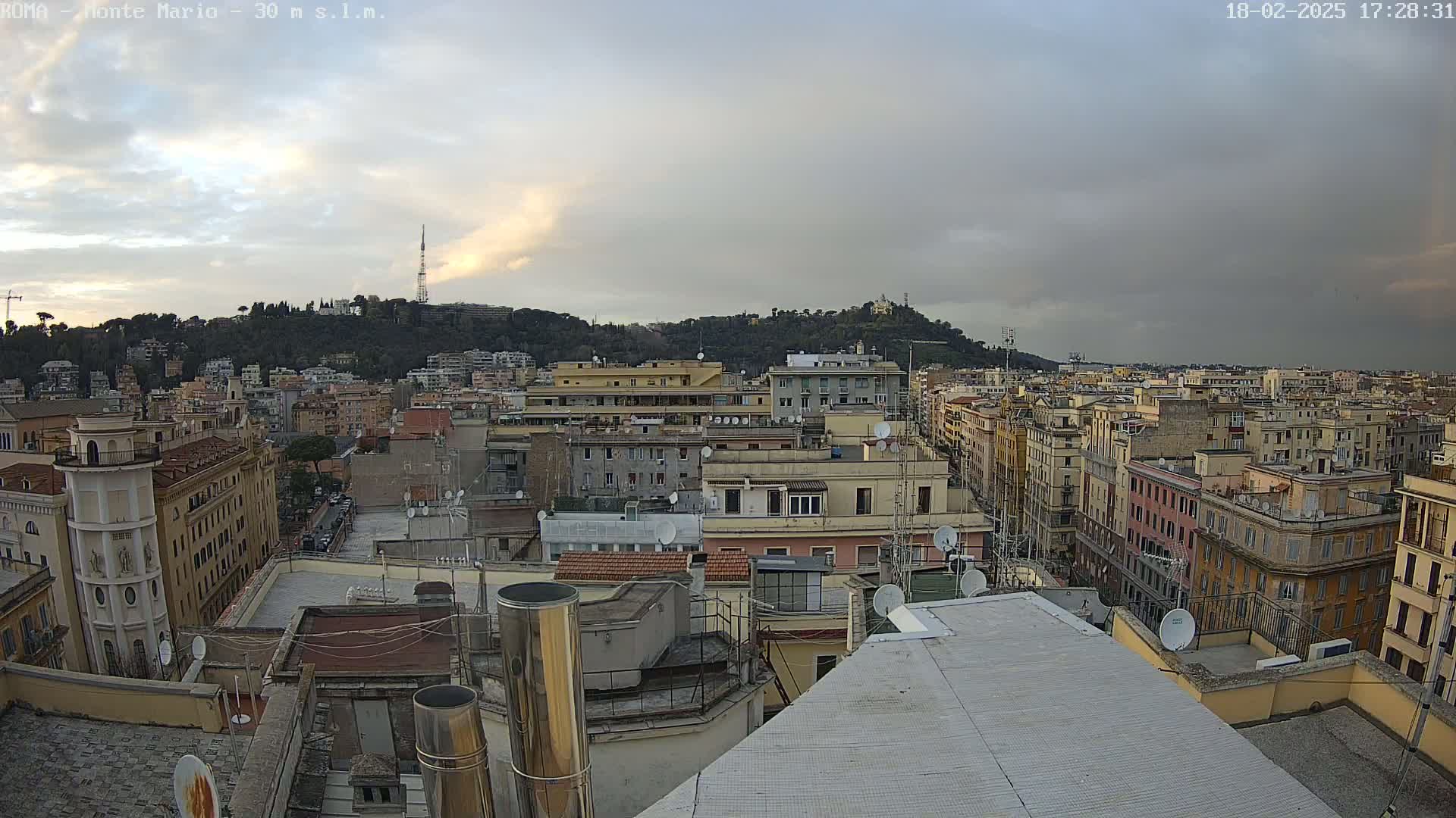 A city skyline with numerous buildings, under an overcast sky with hints of sunset.