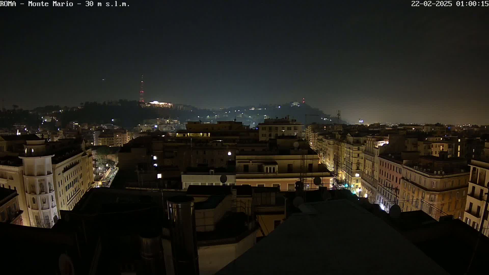 A nighttime aerial view of a city, showing illuminated buildings and streets under a dark, clear sky.