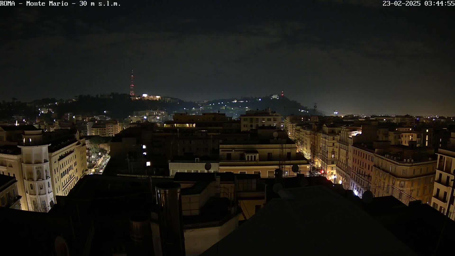 A nighttime view of a city with buildings illuminated, under a mostly clear sky.