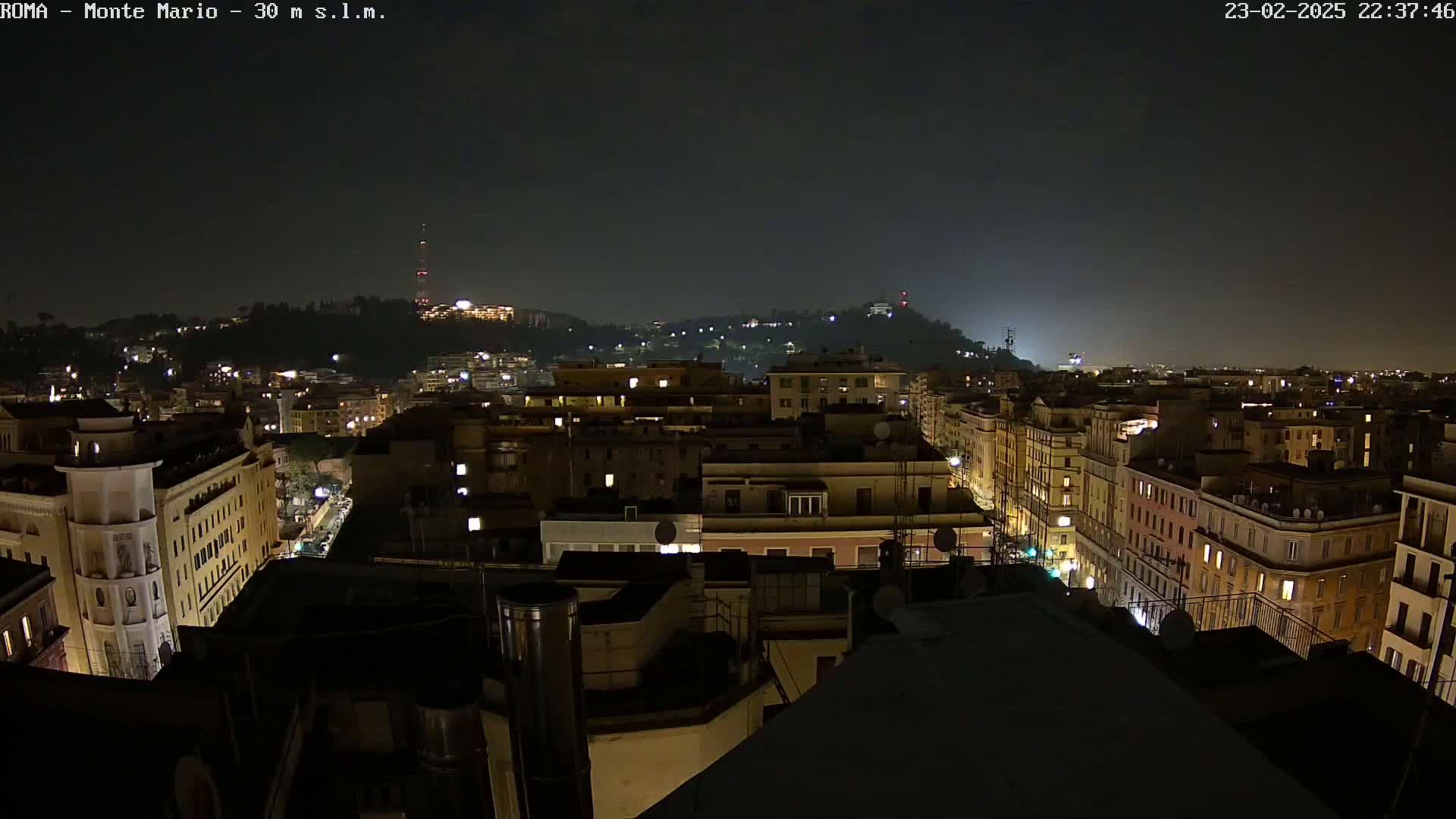 A nighttime view of a city with illuminated buildings extending to a hilltop under a dark sky.
