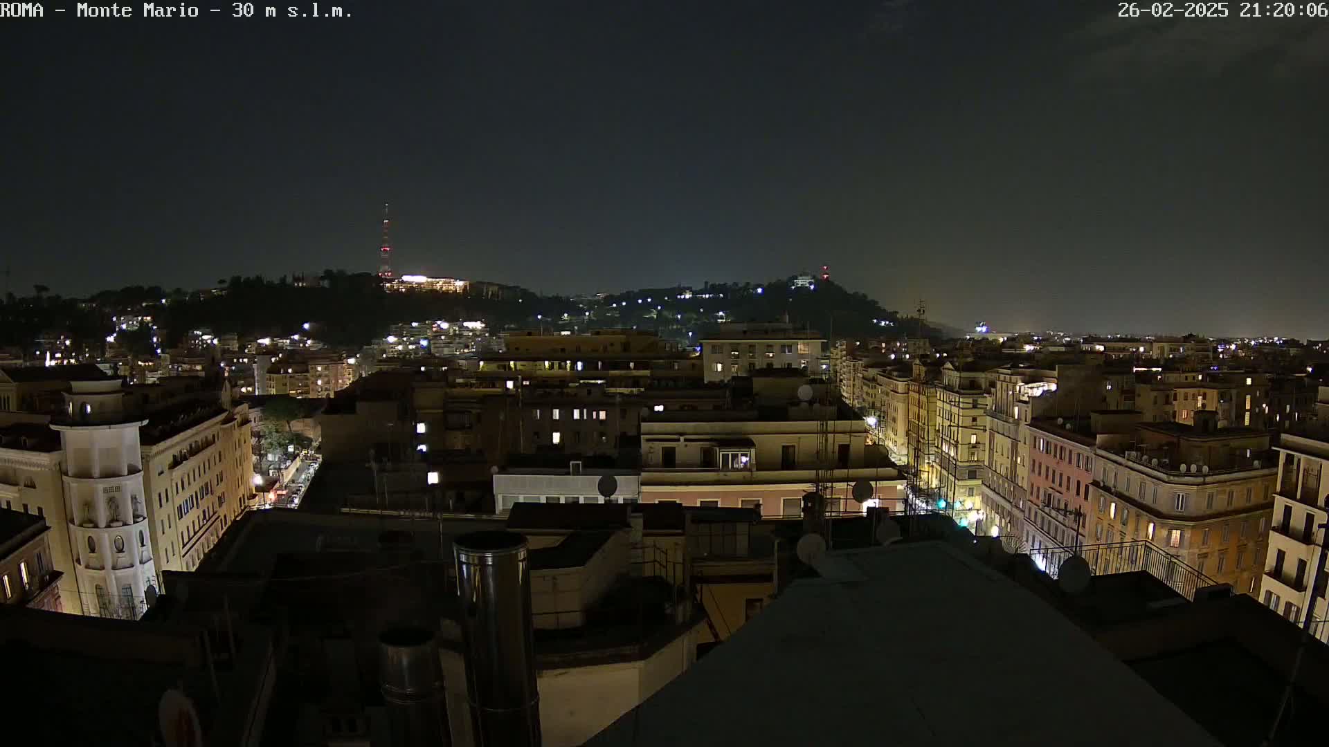 A nighttime, aerial view of a city, showing numerous buildings with illuminated windows, under a dark, clear sky.