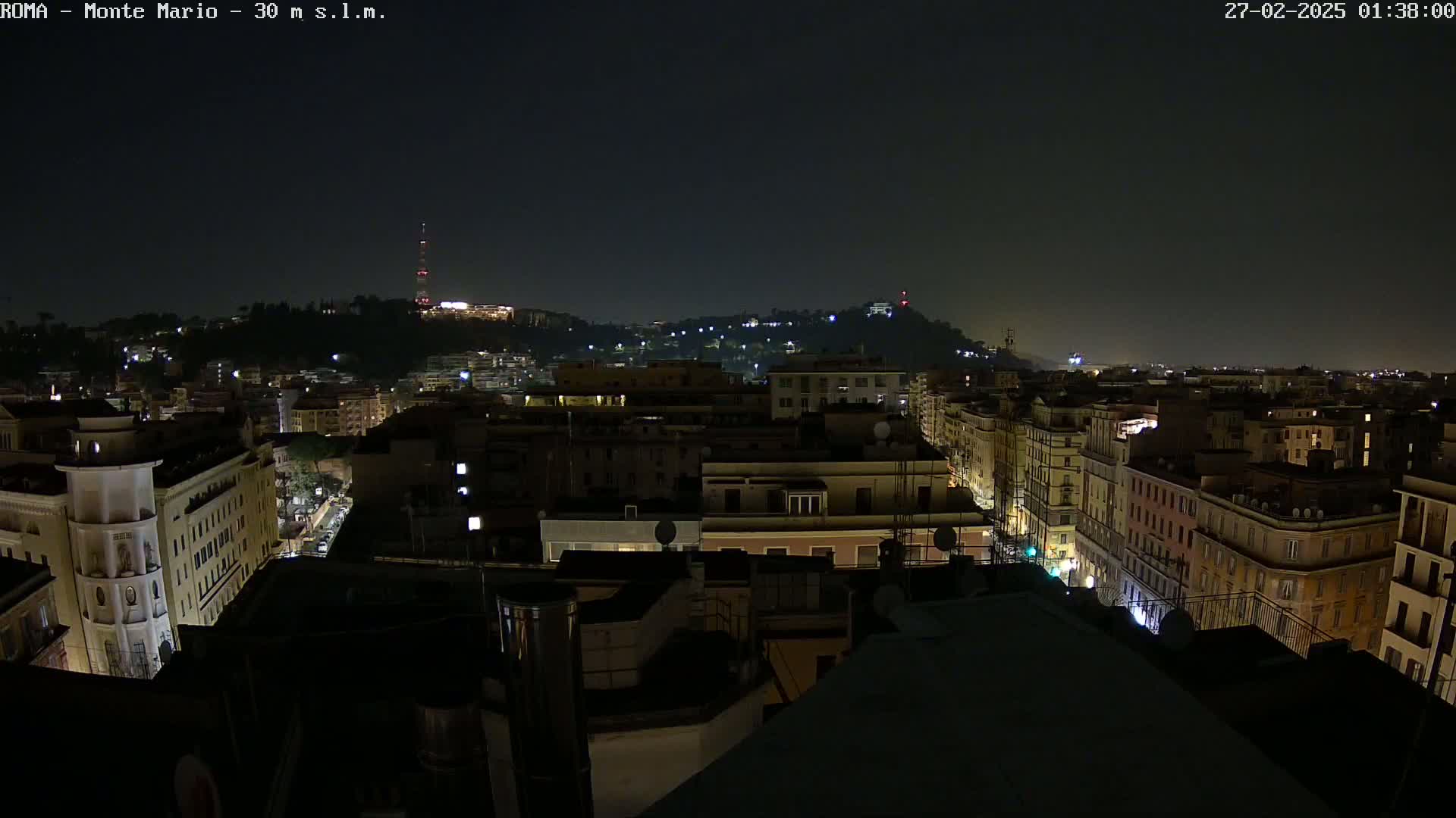 A nighttime view of a city, showing many buildings with scattered lights under a dark sky.