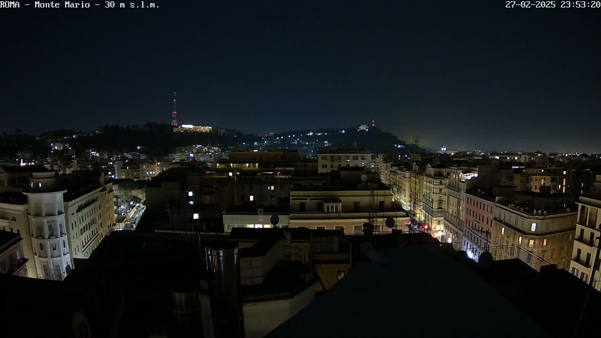 A nighttime view of a city, showing numerous buildings with illuminated windows under a clear, dark sky.
