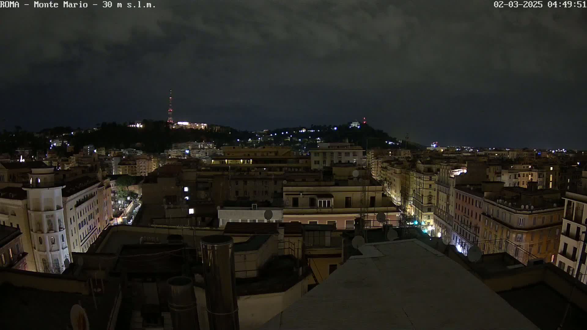 A nighttime view of a city with many buildings illuminated under a dark, cloudy sky.