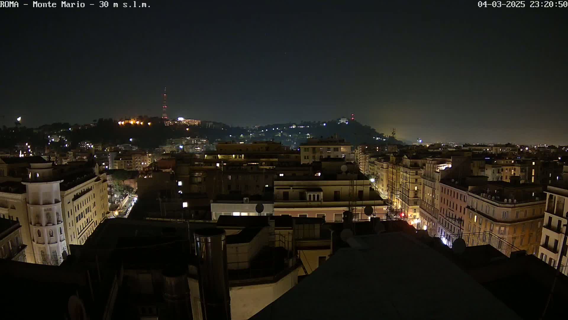 A nighttime view of a city with hills in the background under a dark, clear sky.