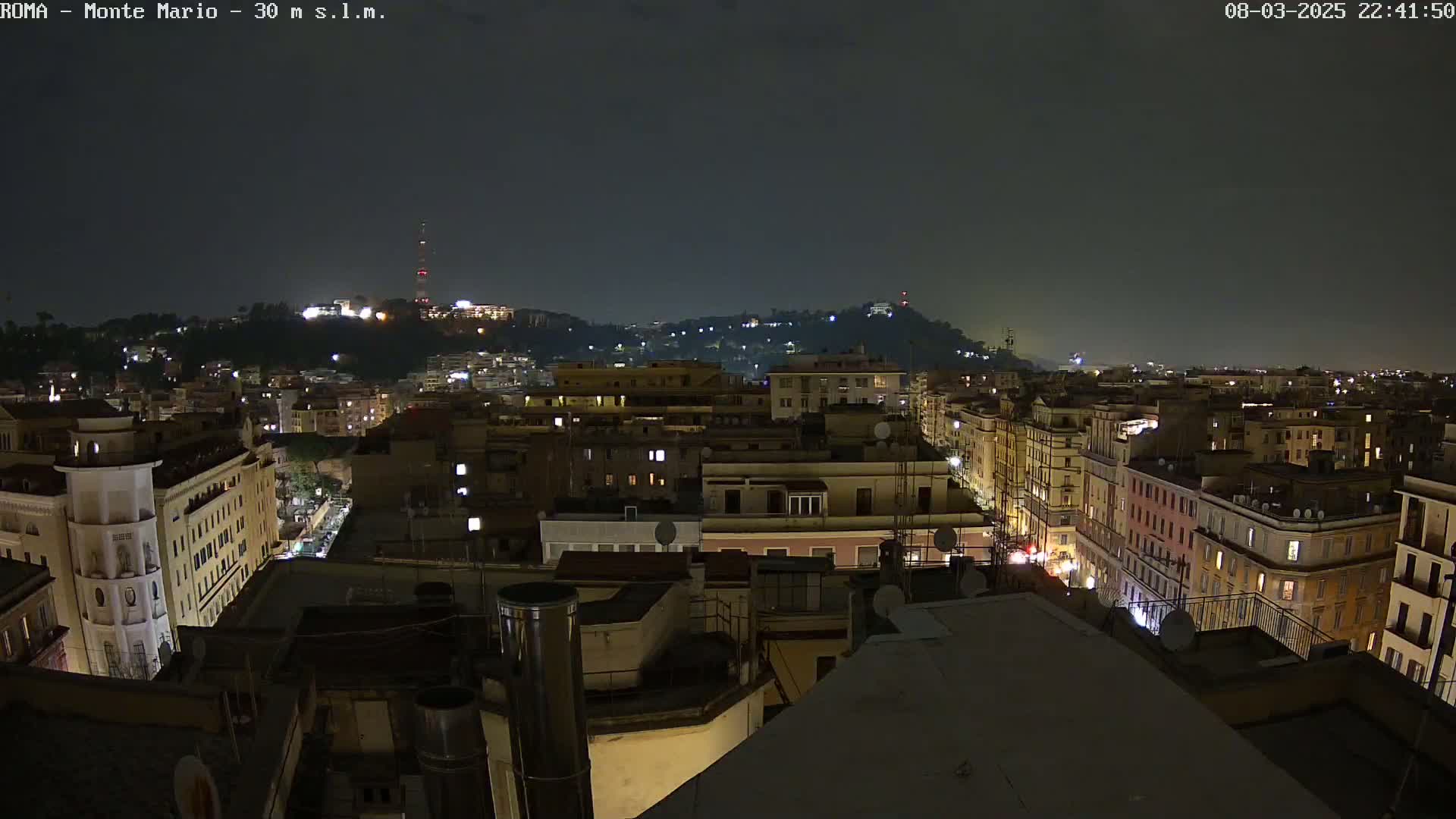 A nighttime cityscape of buildings and hills, under a dark, clear sky.
