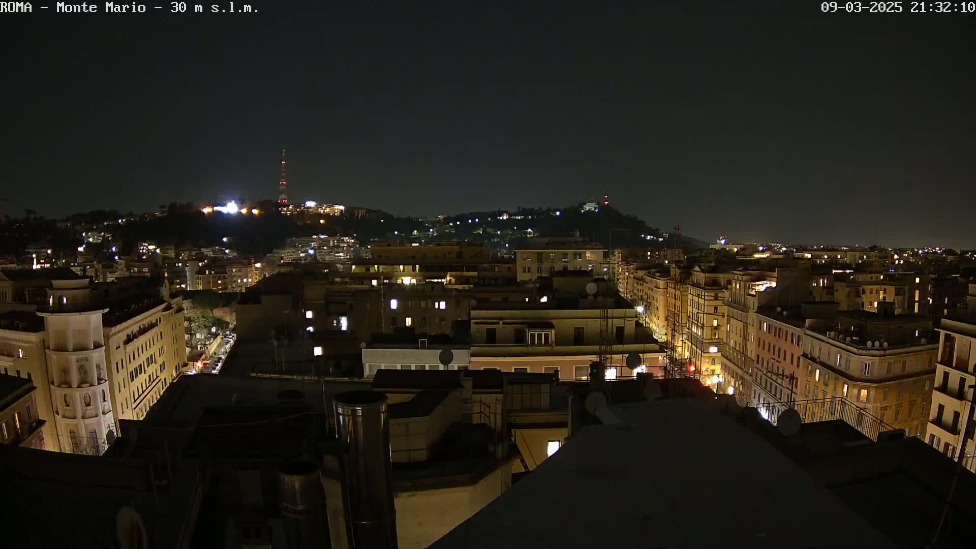 A nighttime, aerial view of a city illuminated by streetlights and building lights, with a hill in the background.