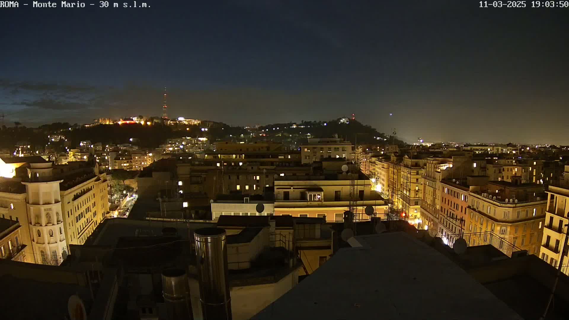 A nighttime view of a city, showing numerous buildings illuminated with lights under a dark, clear sky.