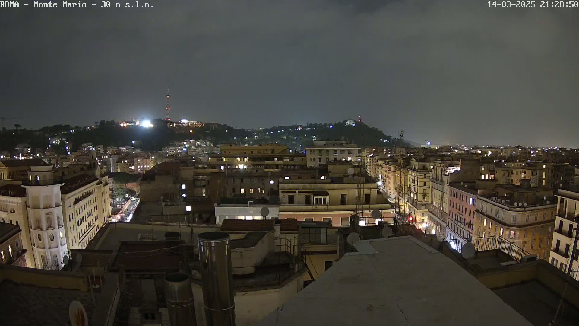 A nighttime view of a city with illuminated buildings under a dark, overcast sky.