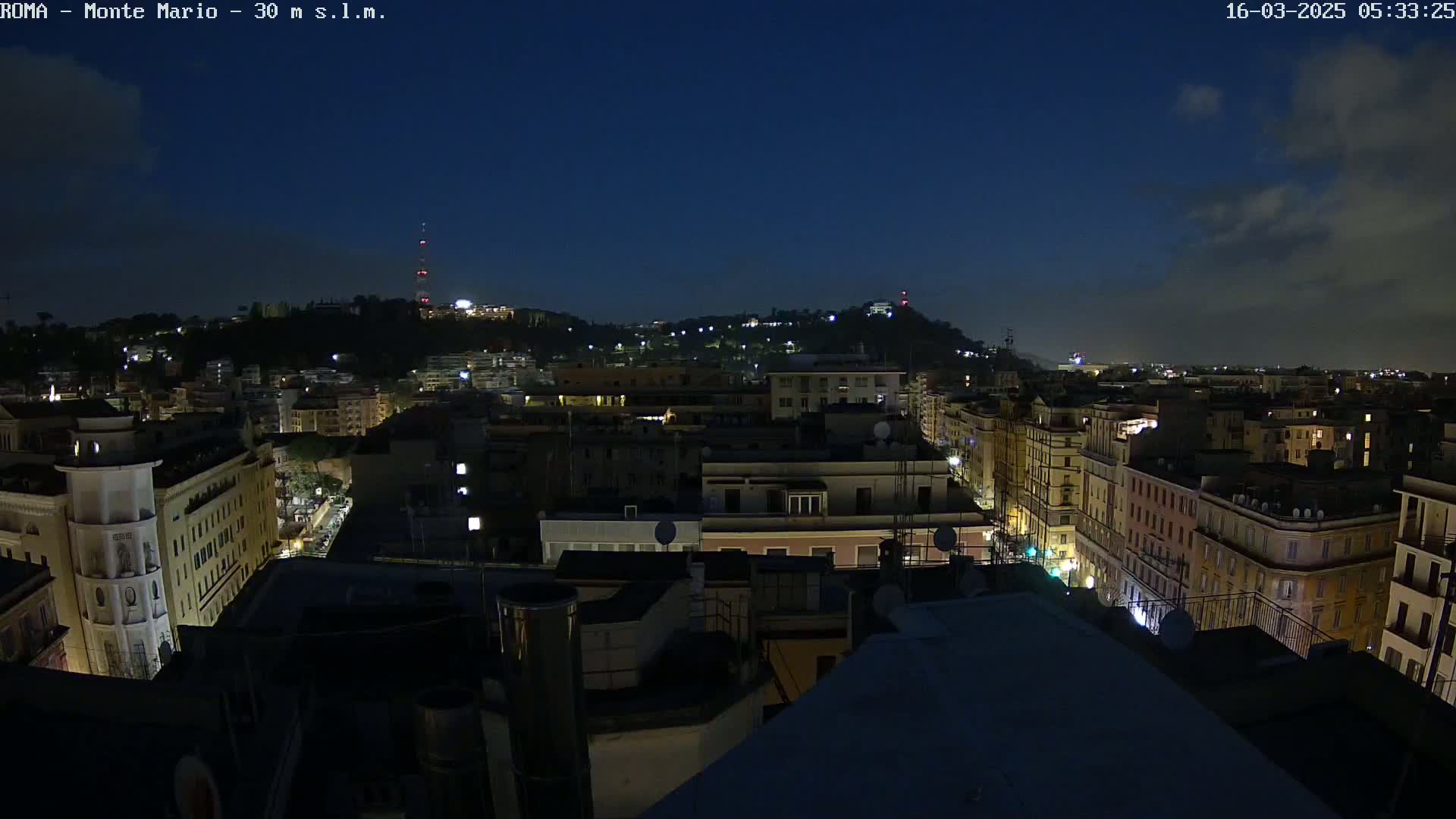 A nighttime view of a city with dimly lit buildings under a dark blue, mostly clear sky.