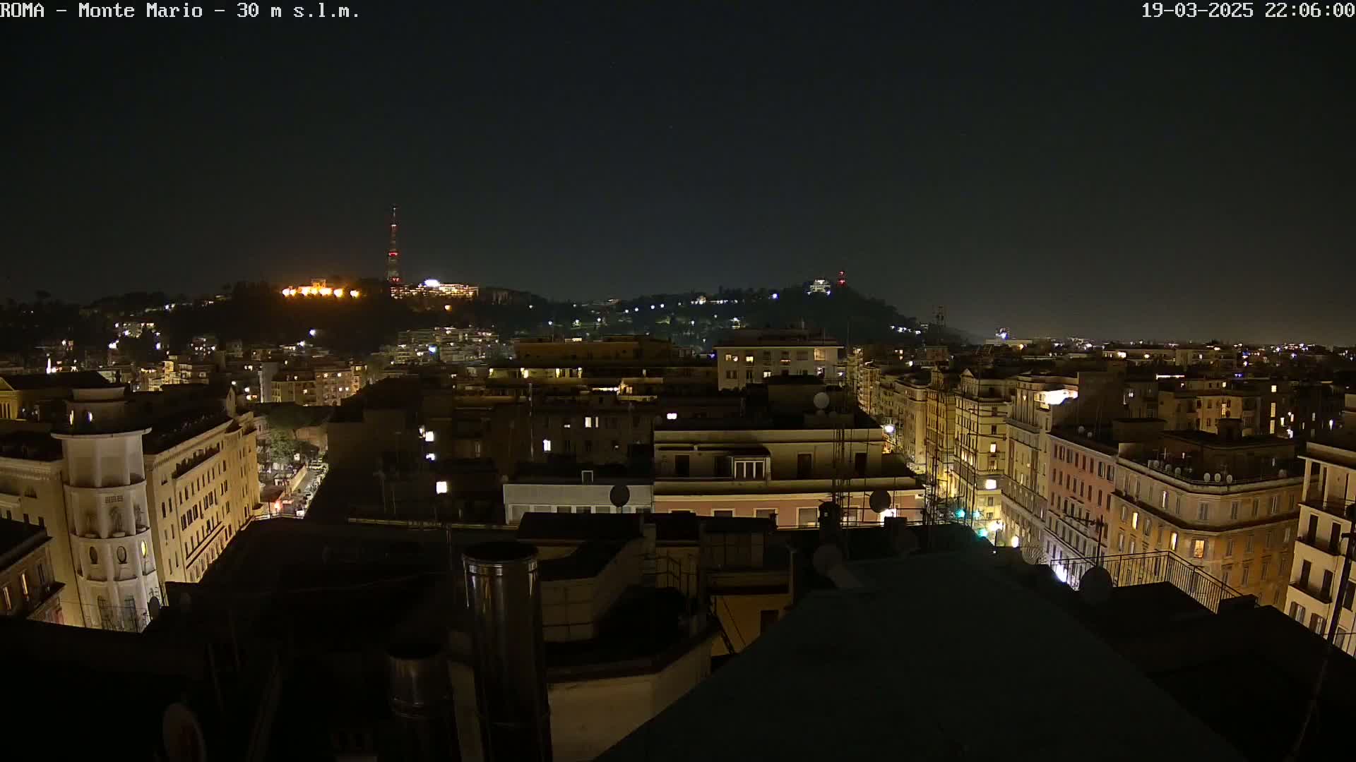 A nighttime view of a city, with a hilltop in the background illuminated by lights.
