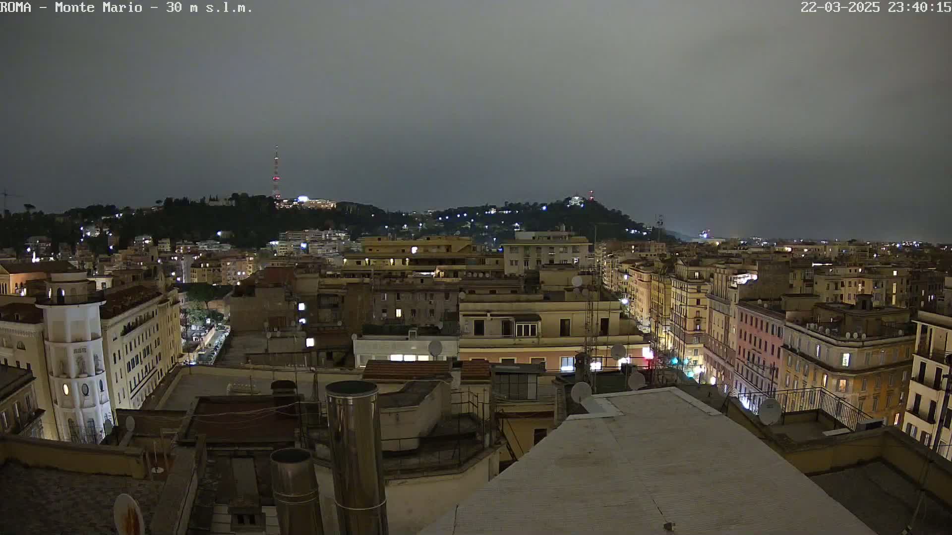 A nighttime view of a city, with many buildings illuminated, under a cloudy, dark sky.