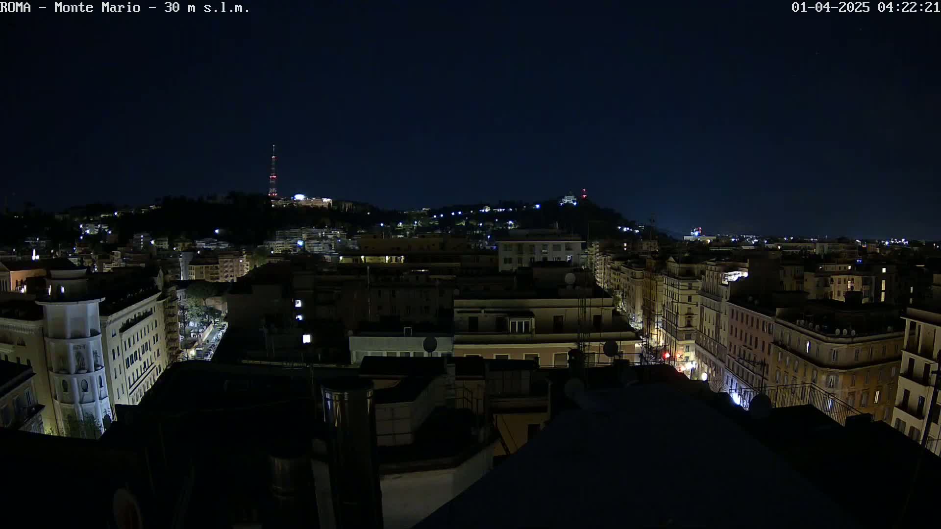 A nighttime view of a city, showing a cityscape illuminated by lights against a dark sky.