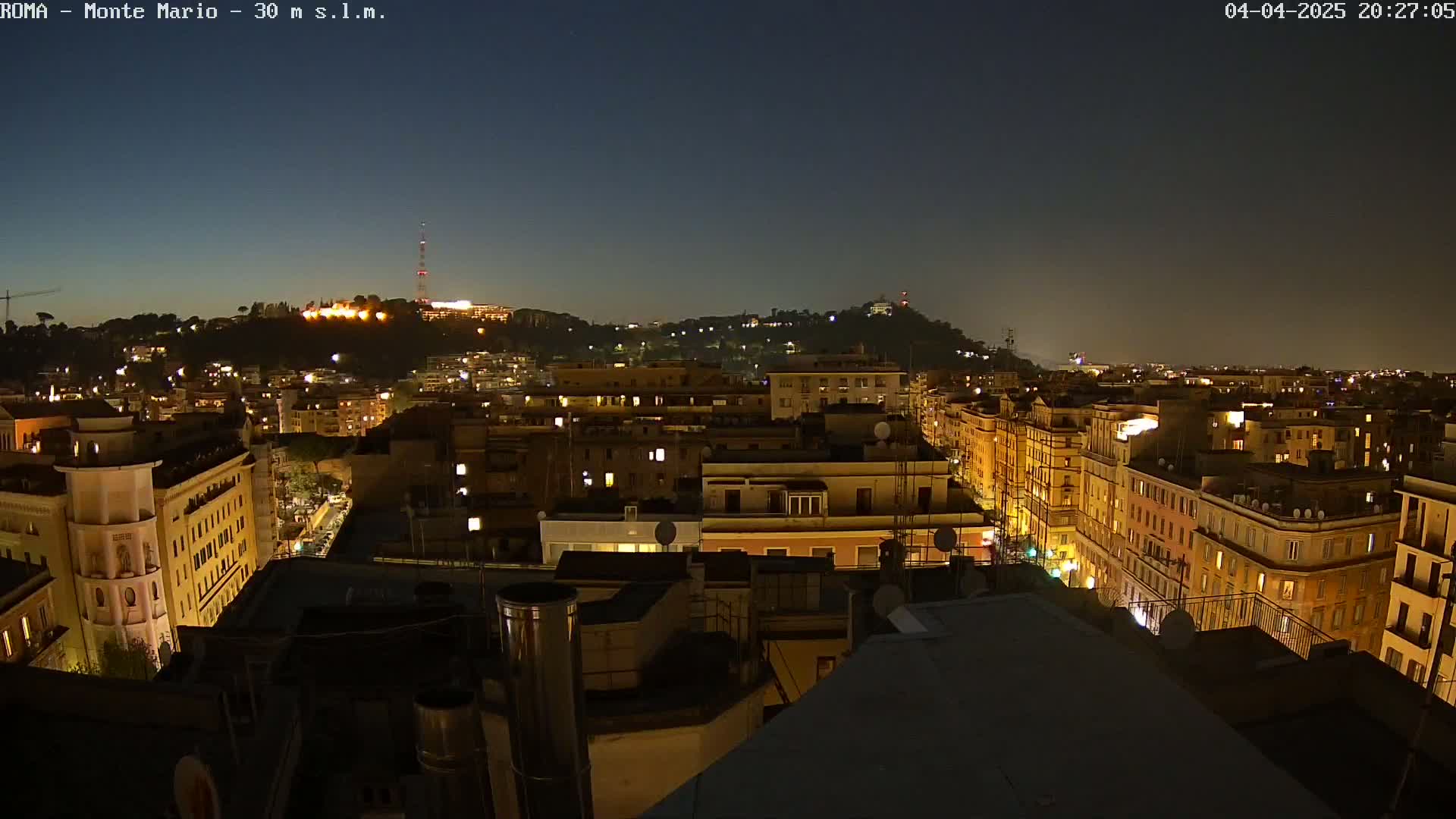 A nighttime view of a city illuminated by lights, with a hill in the background under a clear, dark sky.