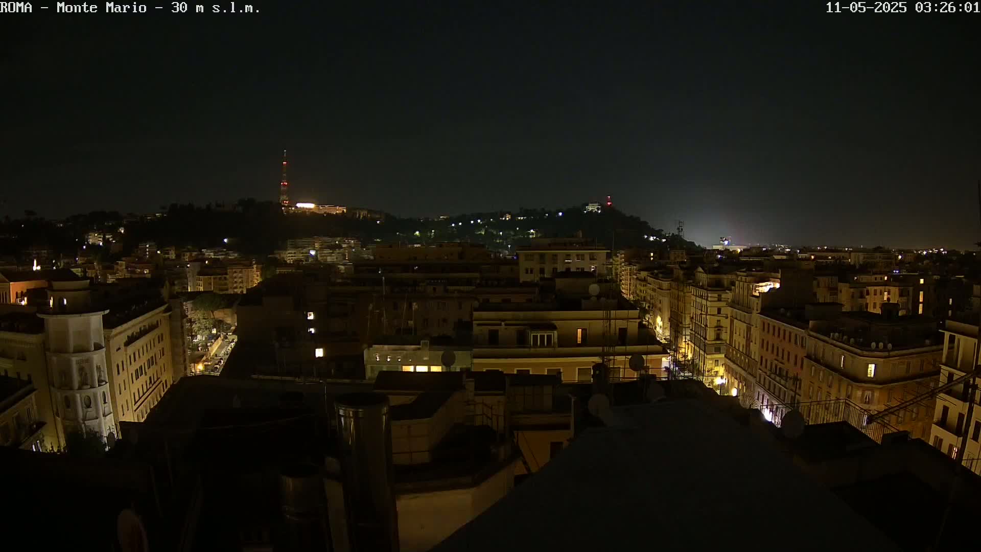 A nighttime aerial view of a city, showing buildings illuminated by interior lights under a dark, clear sky.