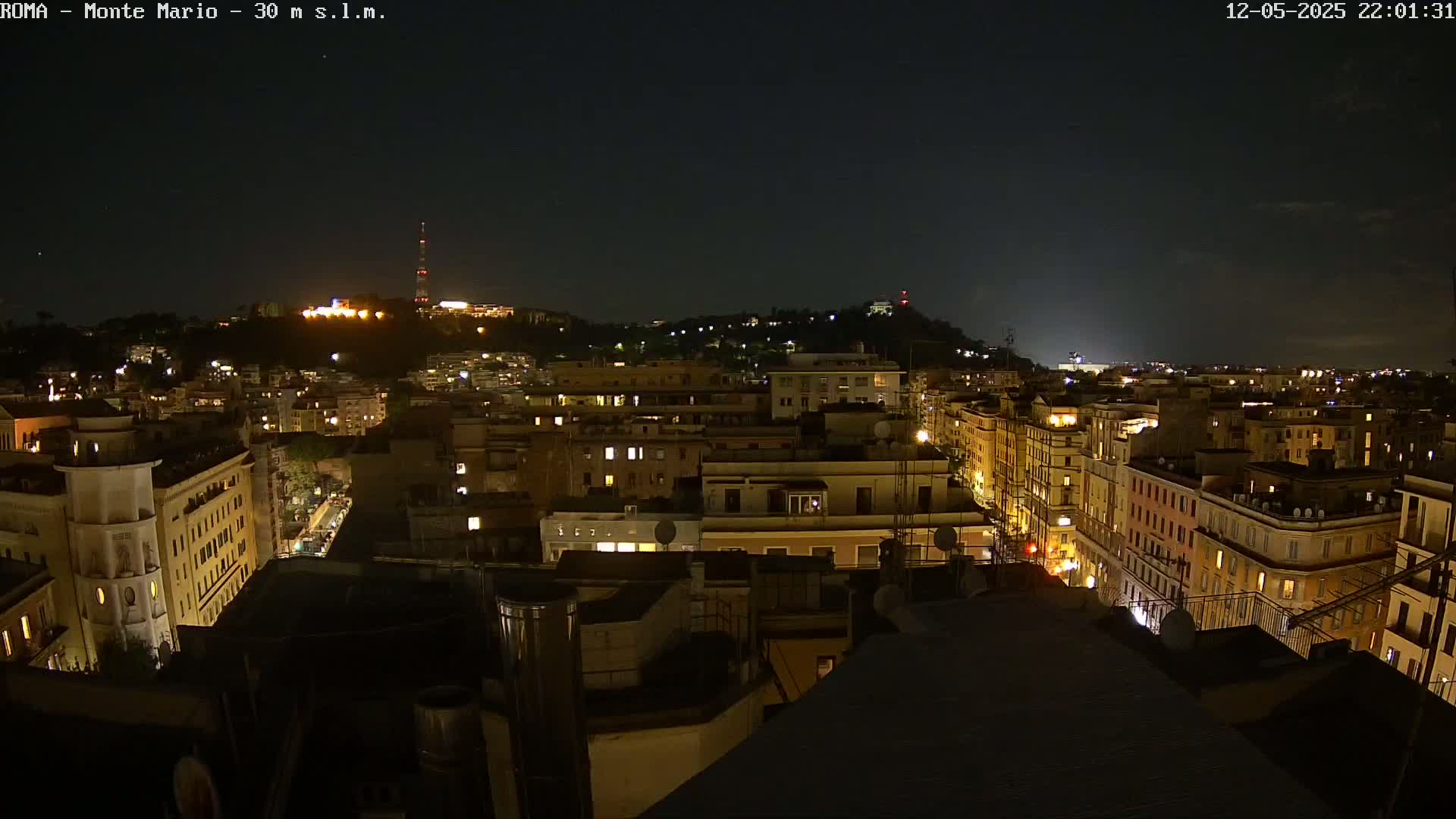 A nighttime view of a city illuminated by many lights, with a hill in the background under a clear sky.
